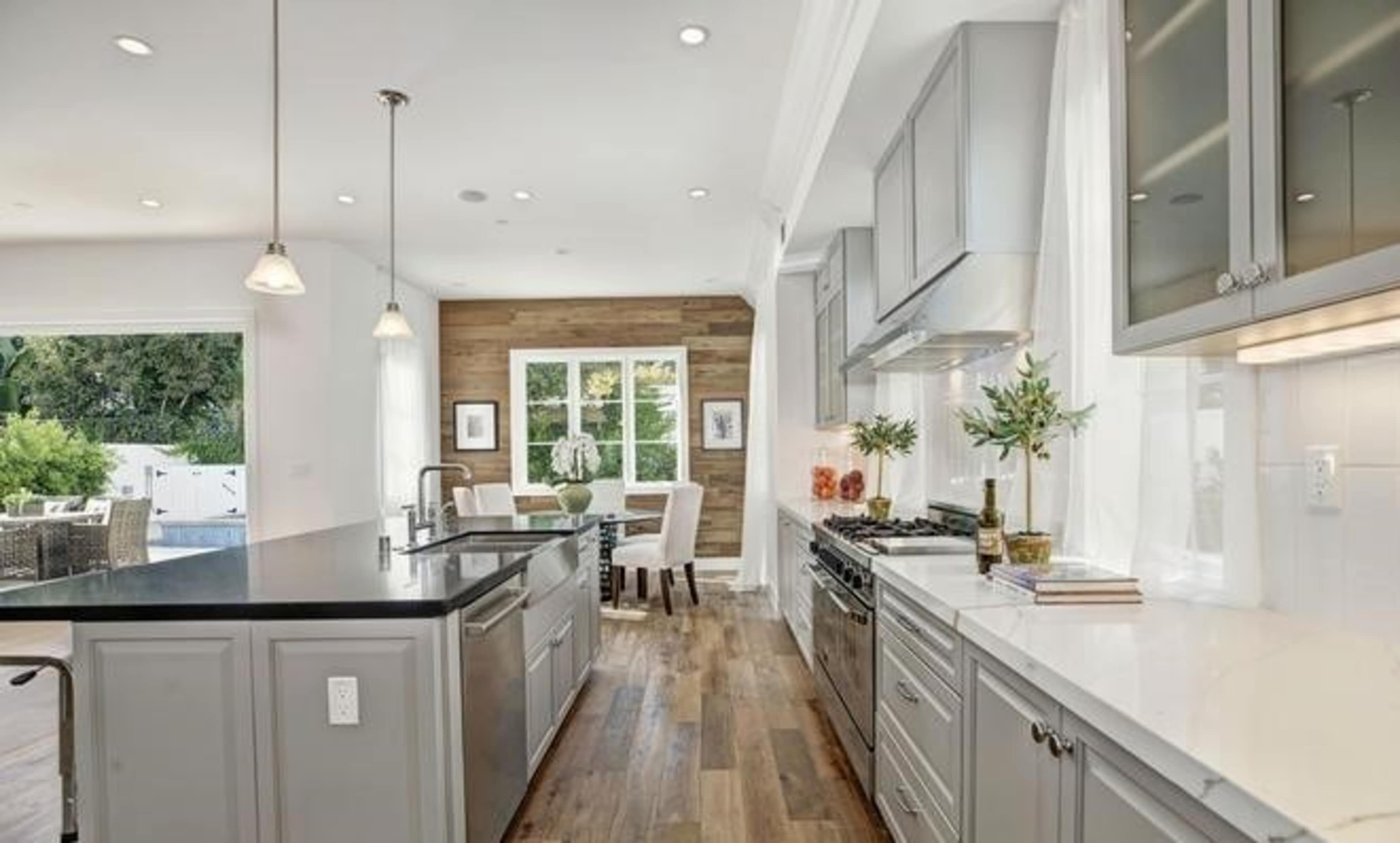 A modern kitchen features stainless steel appliances, a large island with a dark countertop, and a dining area with a wooden accent wall.
