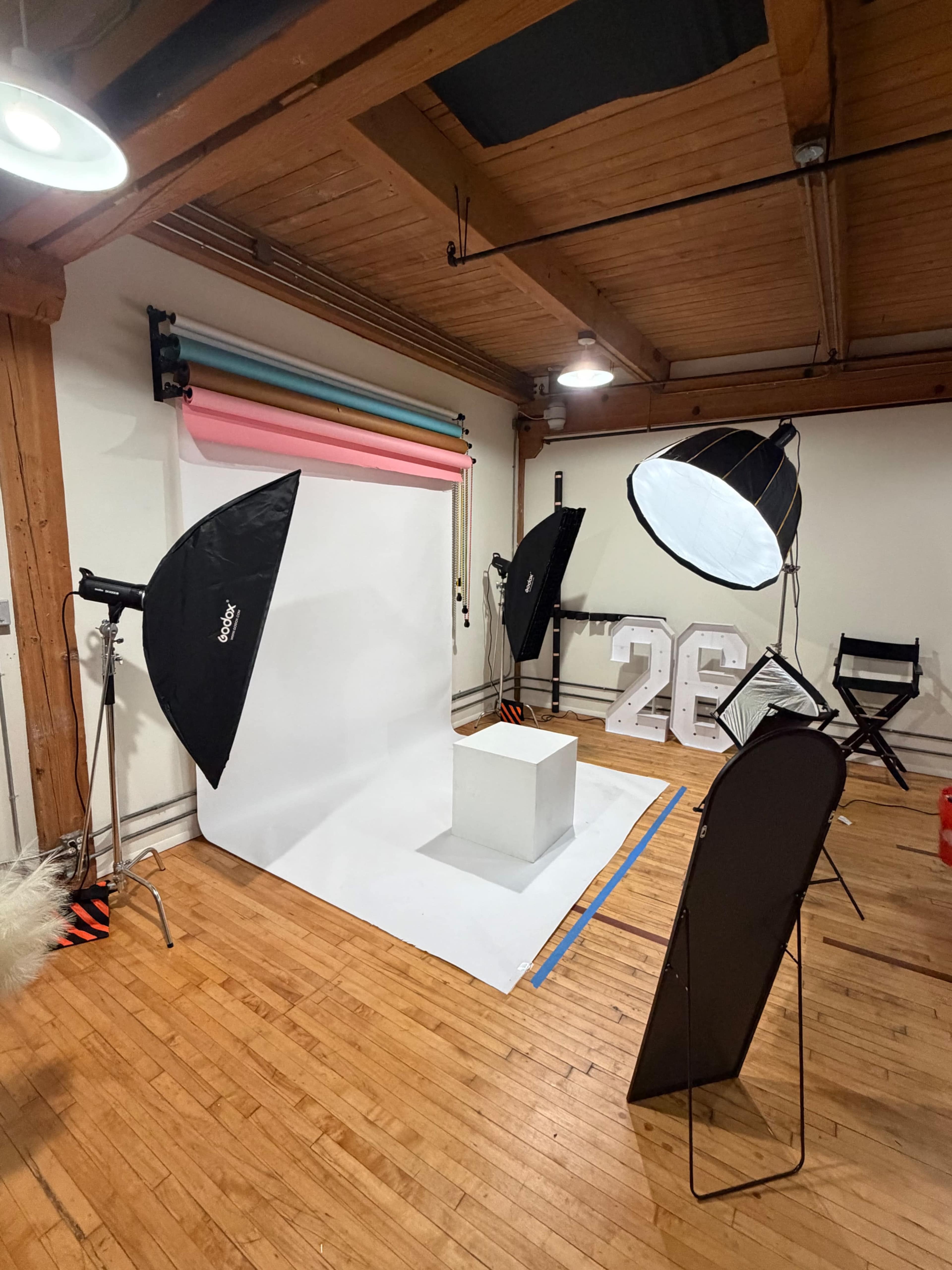 The image shows a photography studio setup with various backdrops, lighting equipment, and a white display pedestal.