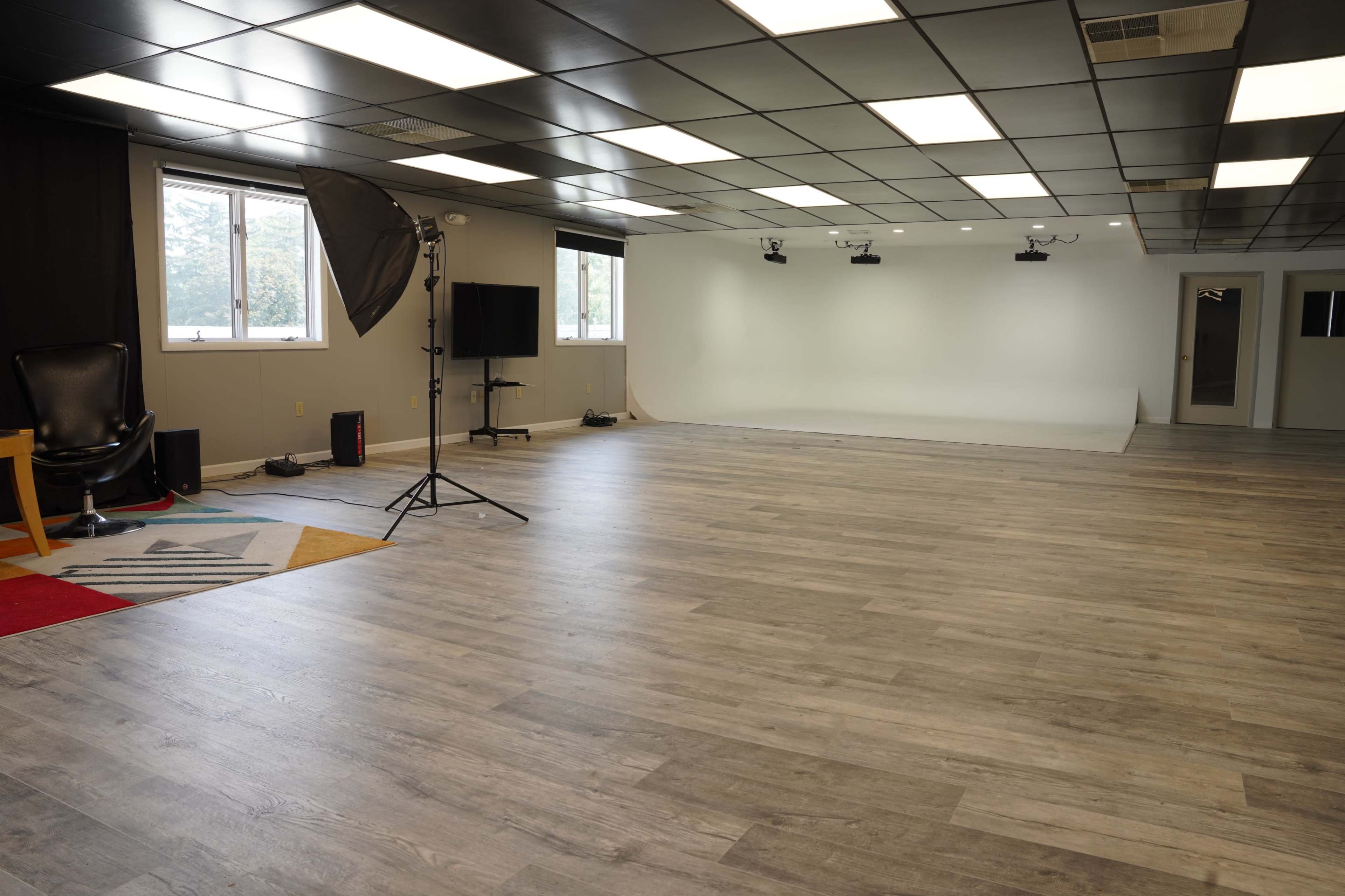 A spacious studio with wooden floors, soft lighting, and a backdrop area equipped for photography or videography.
