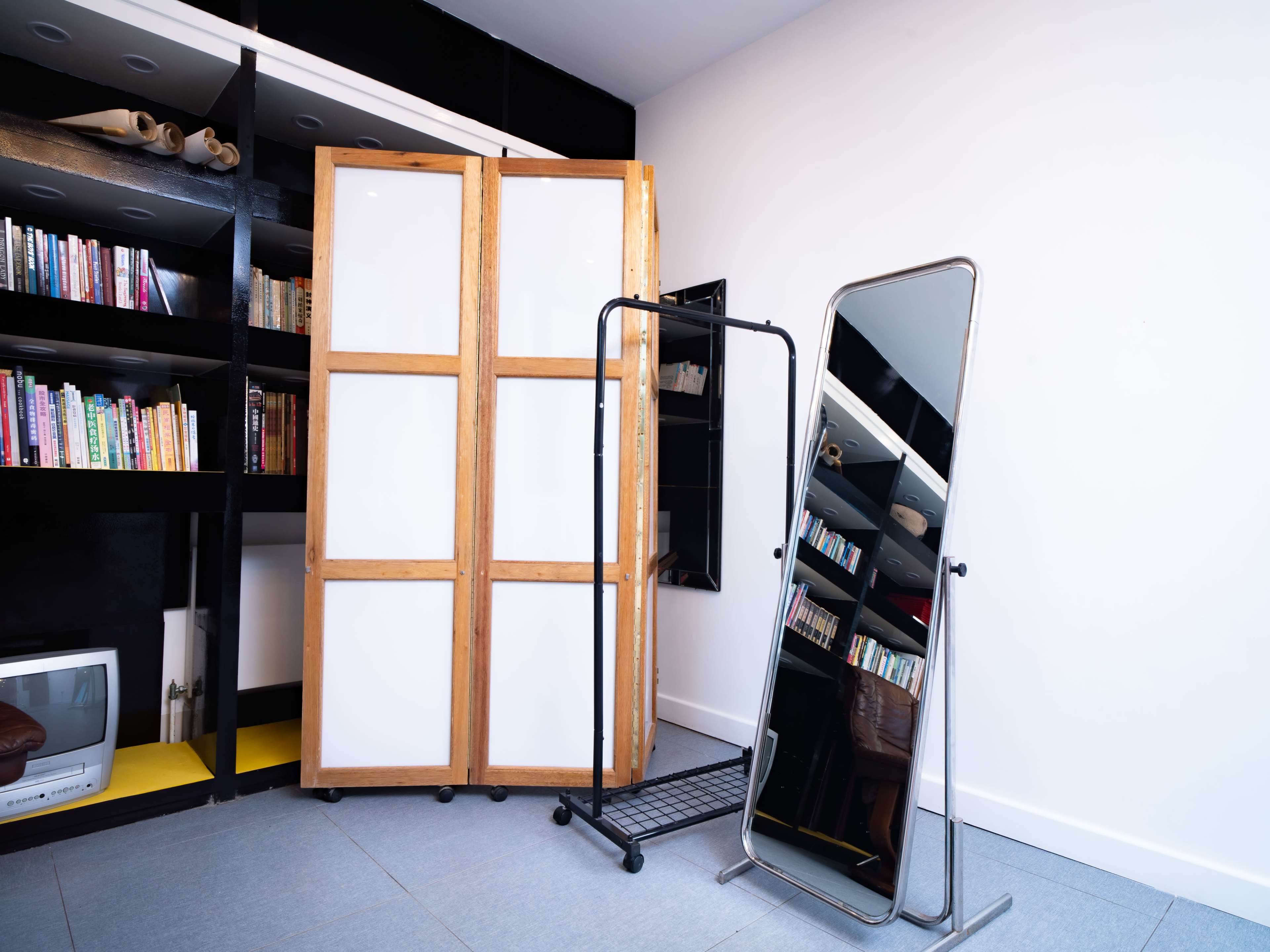 The image shows a room with a bookshelf filled with books, a wooden screen, and two standing mirrors.