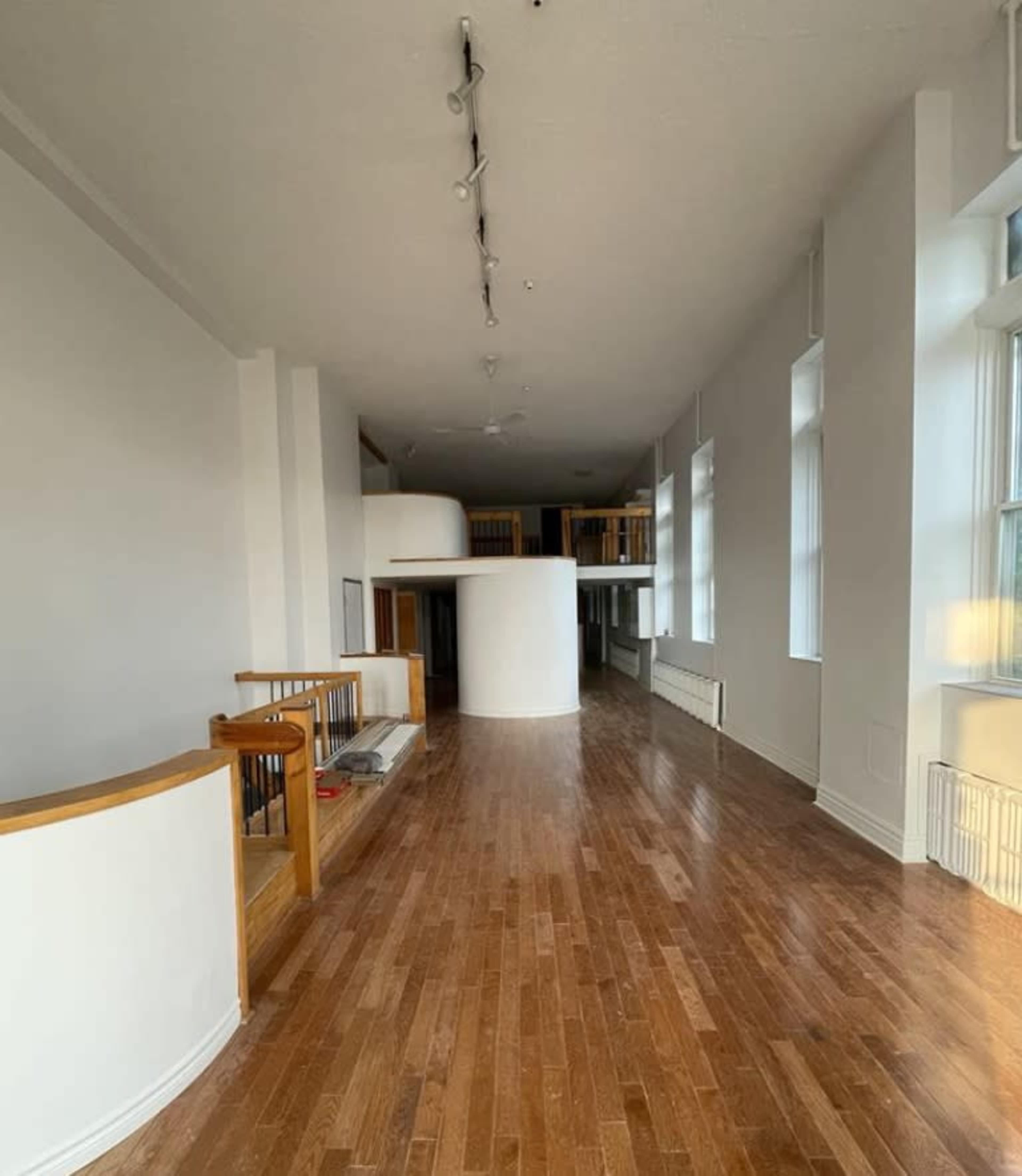 The image shows a spacious interior of a modern building with hardwood flooring, large windows, and a curved white wall.