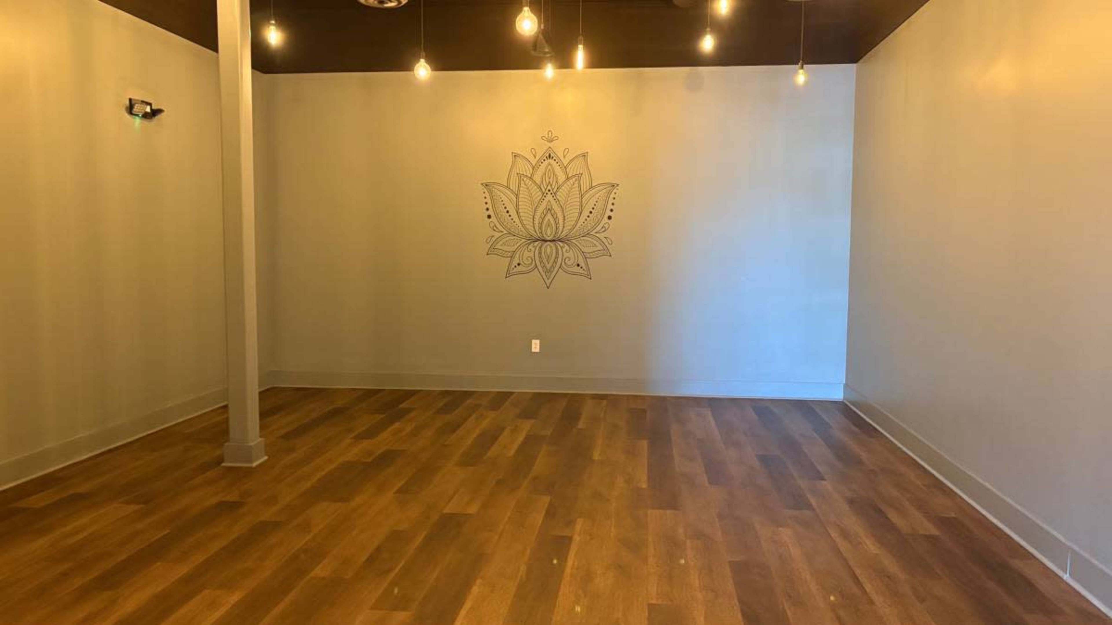 The room features a wooden floor and a large lotus mural on a light gray wall, illuminated by pendant lights hanging from the ceiling.