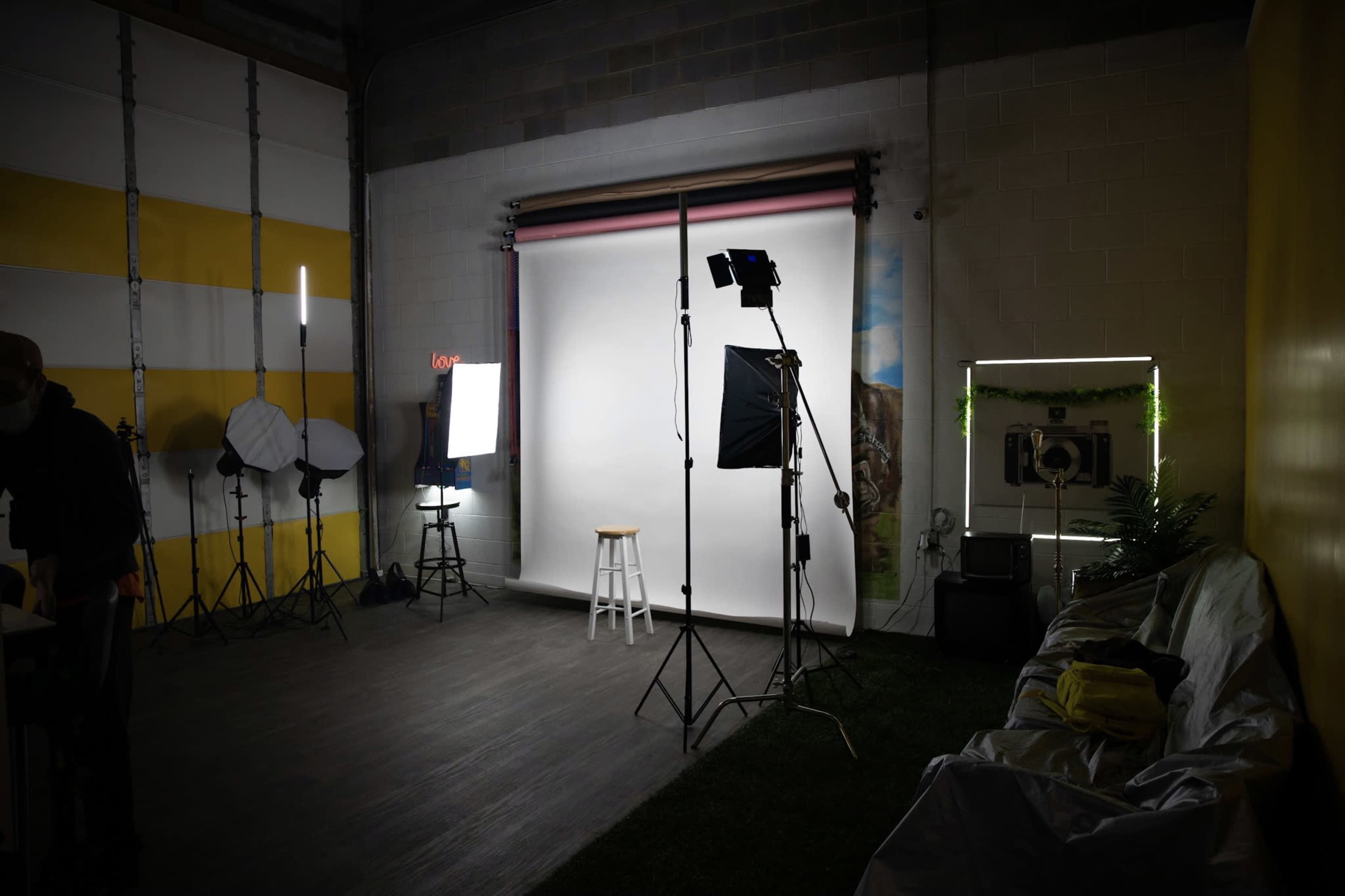 A photography studio is set up with lighting equipment, a backdrop, and a stool in an organized space.