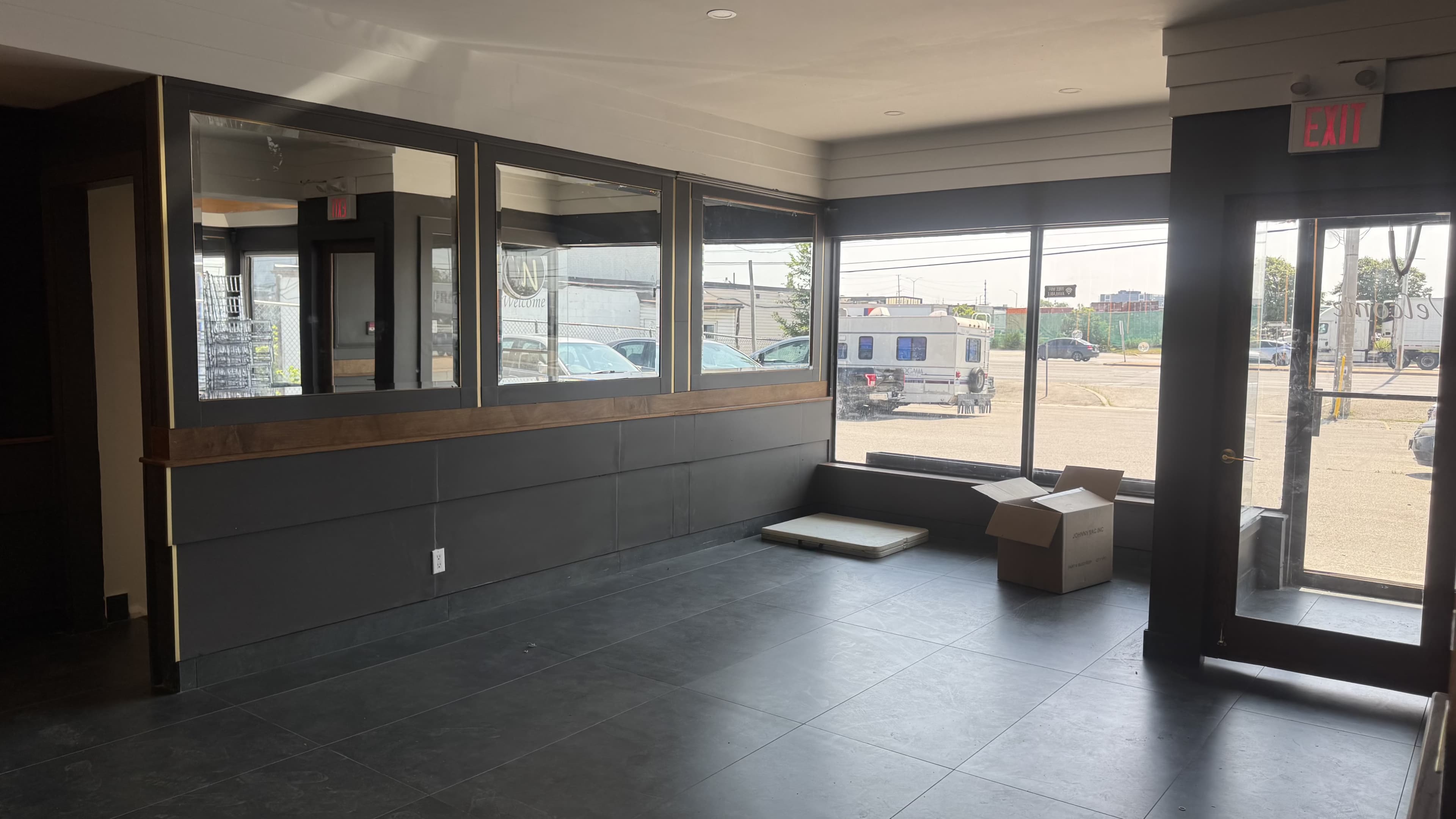 The image shows an empty commercial space with large windows, a glass entrance door, and a cardboard box on the floor.
