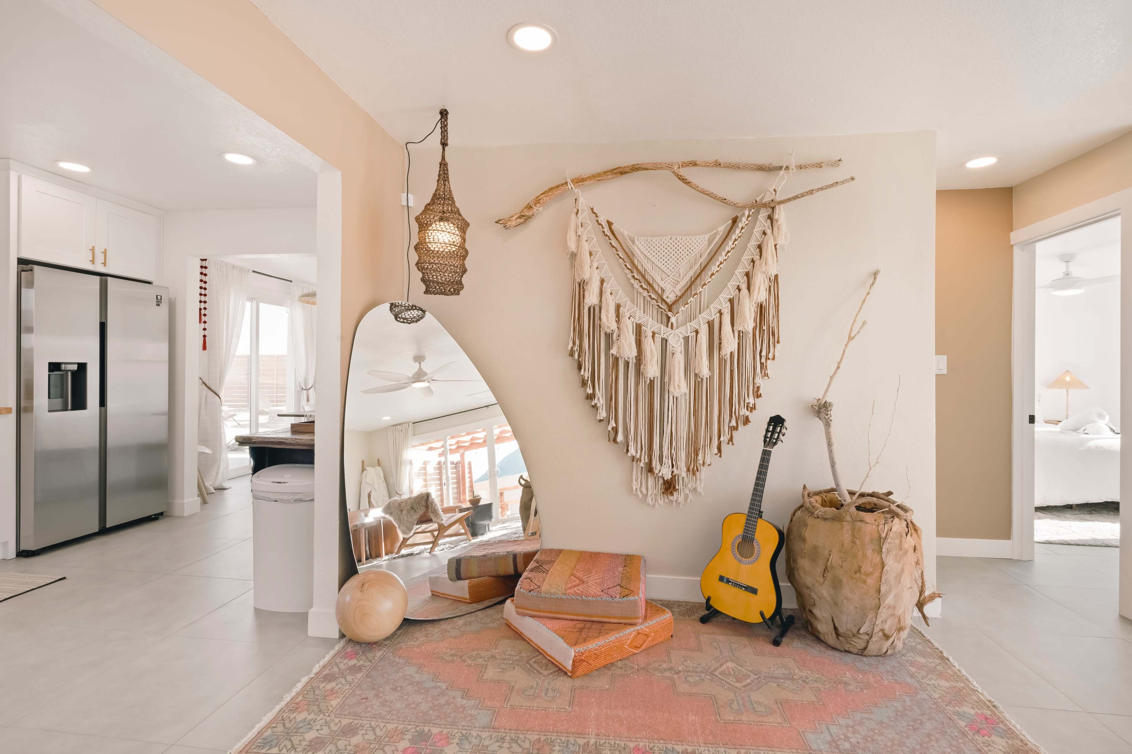 The scene features a cozy indoor space with a decorative macramé wall hanging, a guitar, a mirror, and a large woven basket, set against a light-colored wall and a patterned rug.
