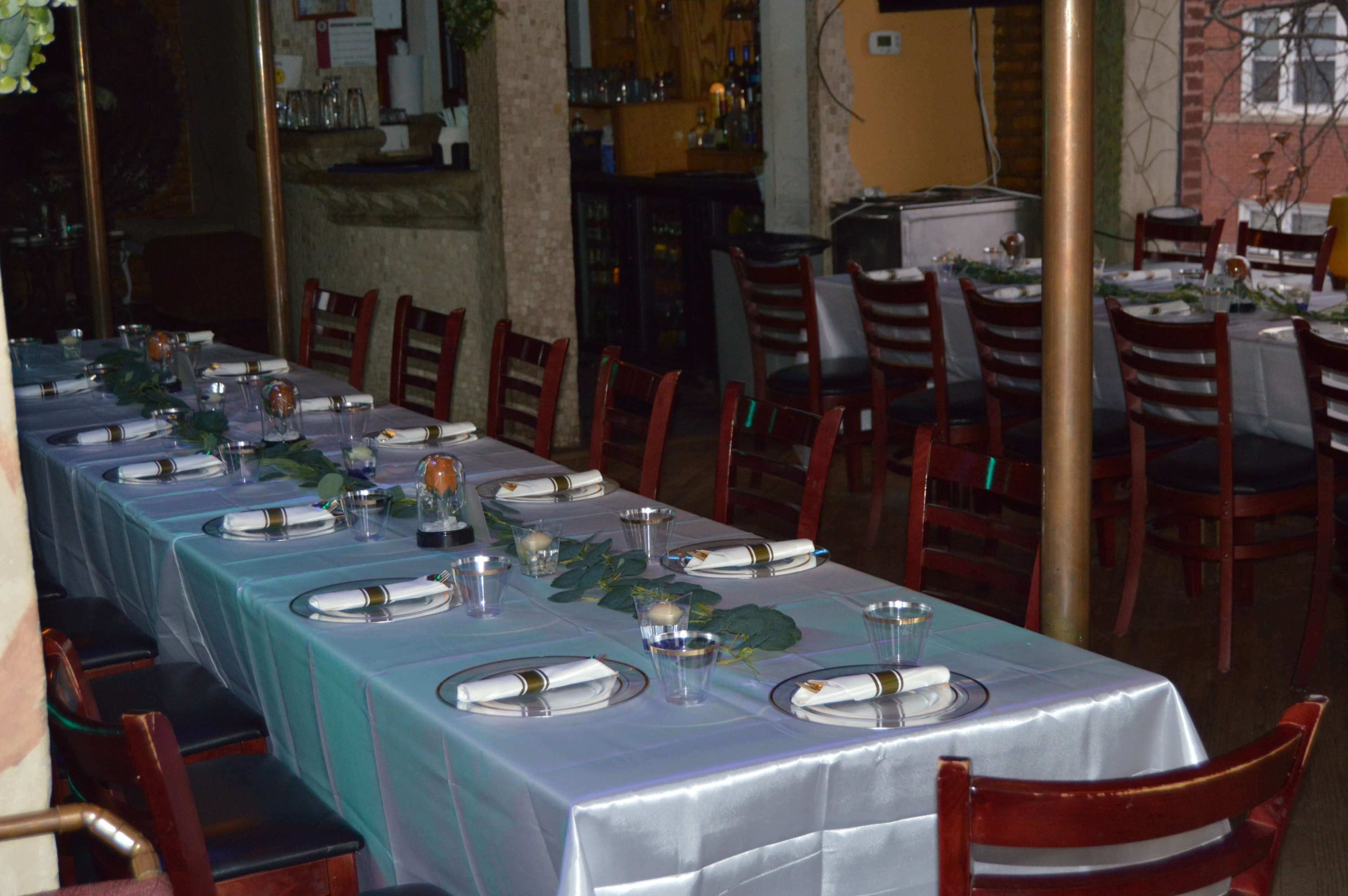 A long, neatly arranged dining table is set with plates, glasses, and silverware in a restaurant.