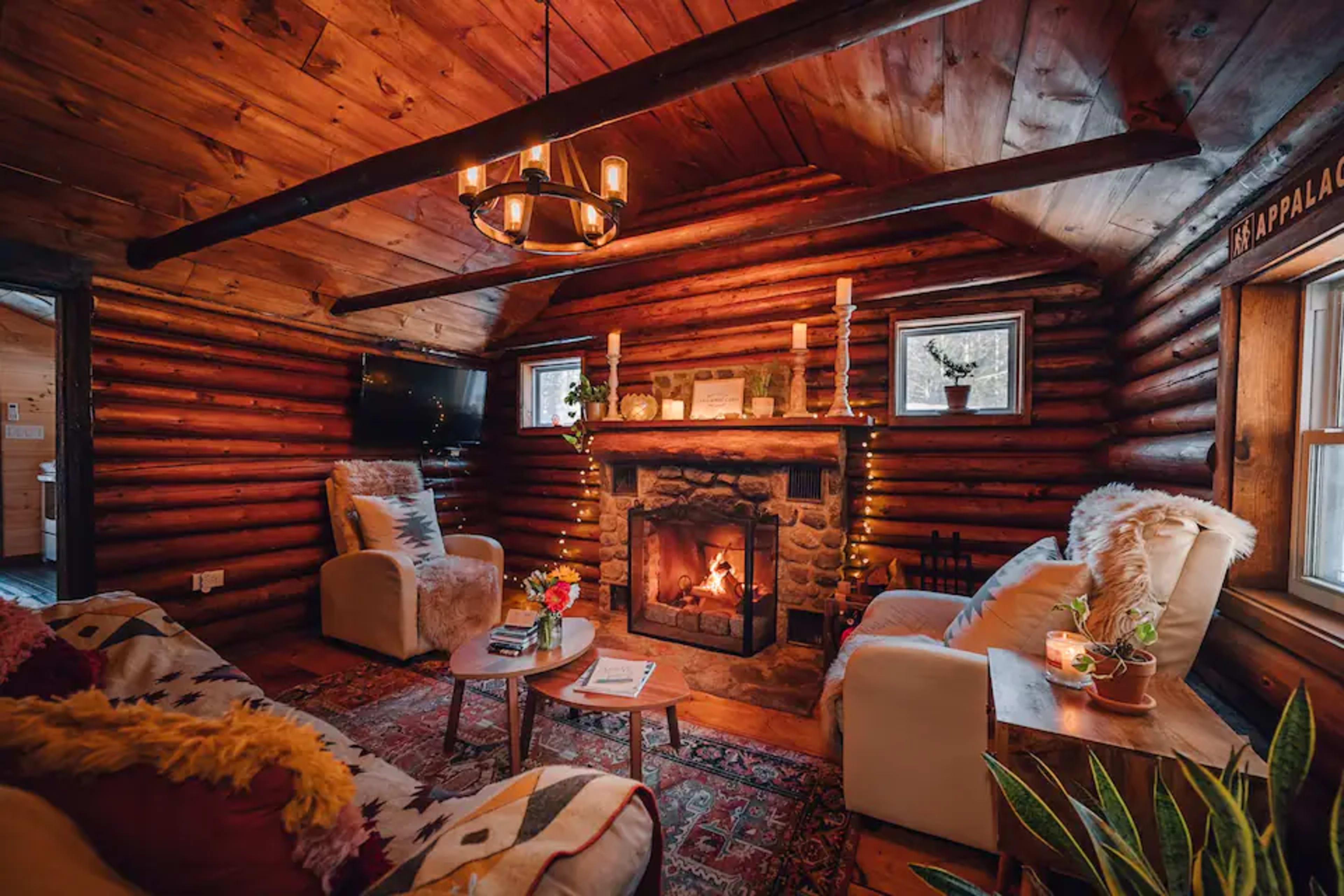 A cozy log cabin interior with a stone fireplace, two armchairs, and a wooden ceiling.