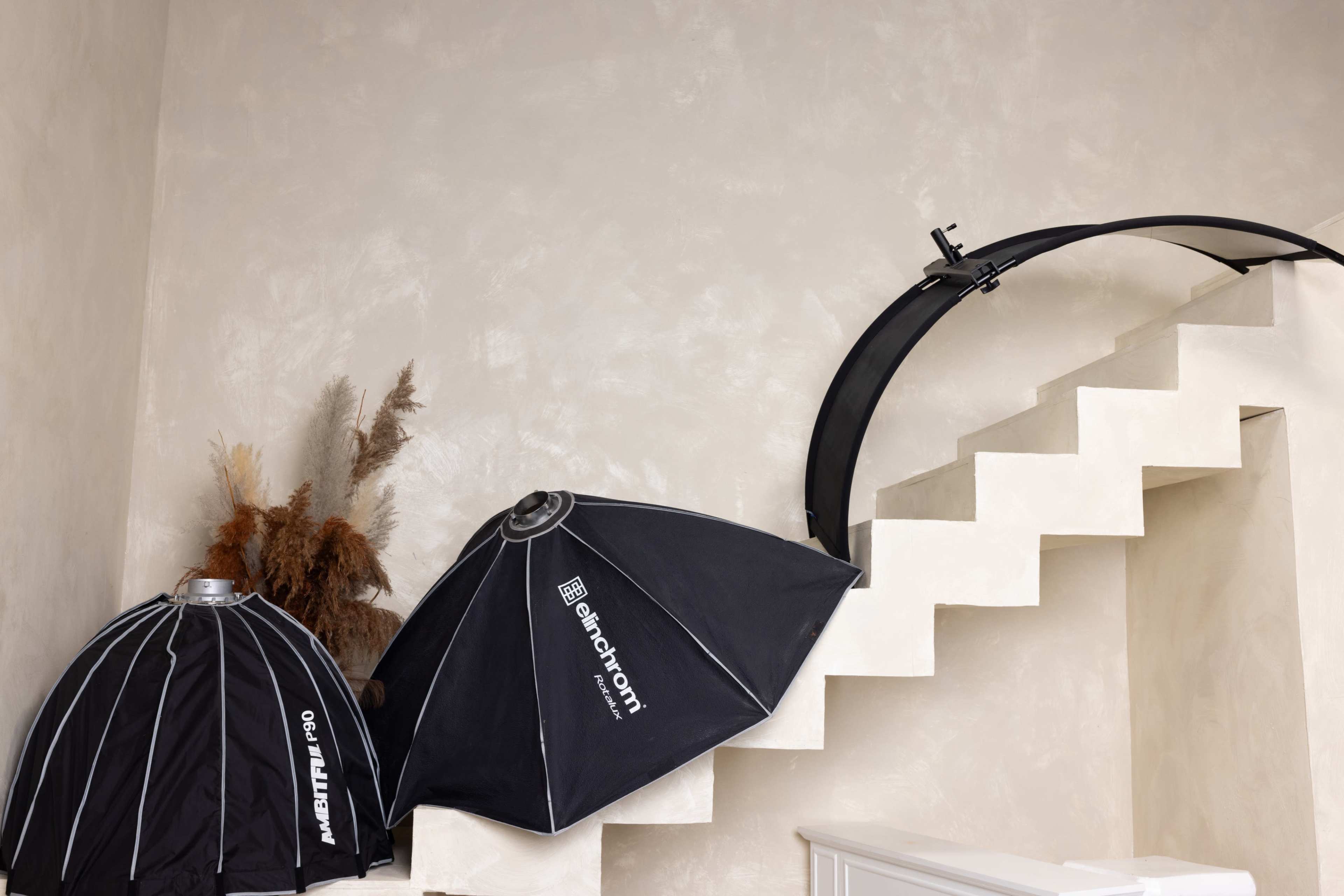 Two photography light umbrellas and a curved light mount positioned near a staircase against a textured wall.