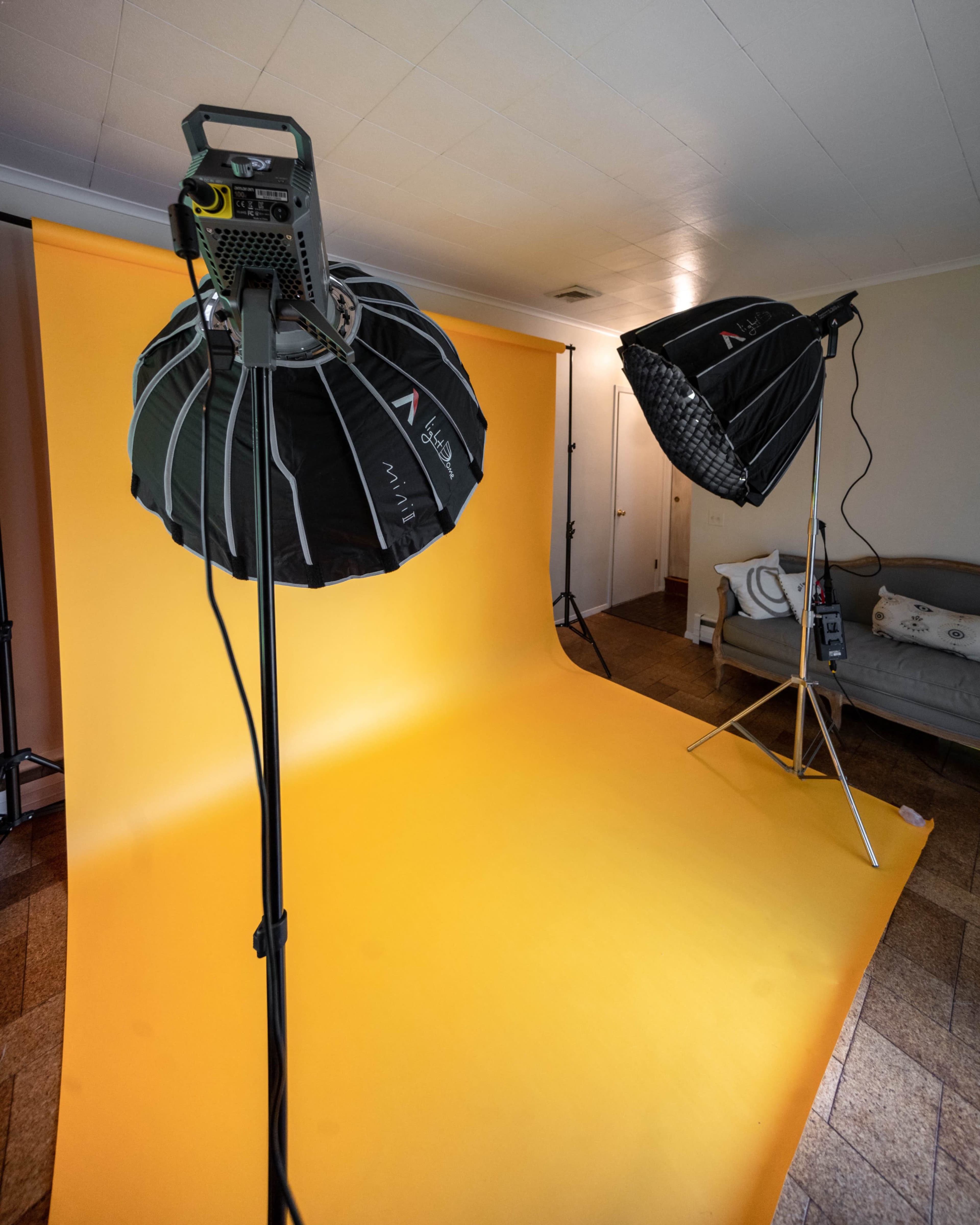 A photography studio setup with two softbox lights positioned above a yellow backdrop.