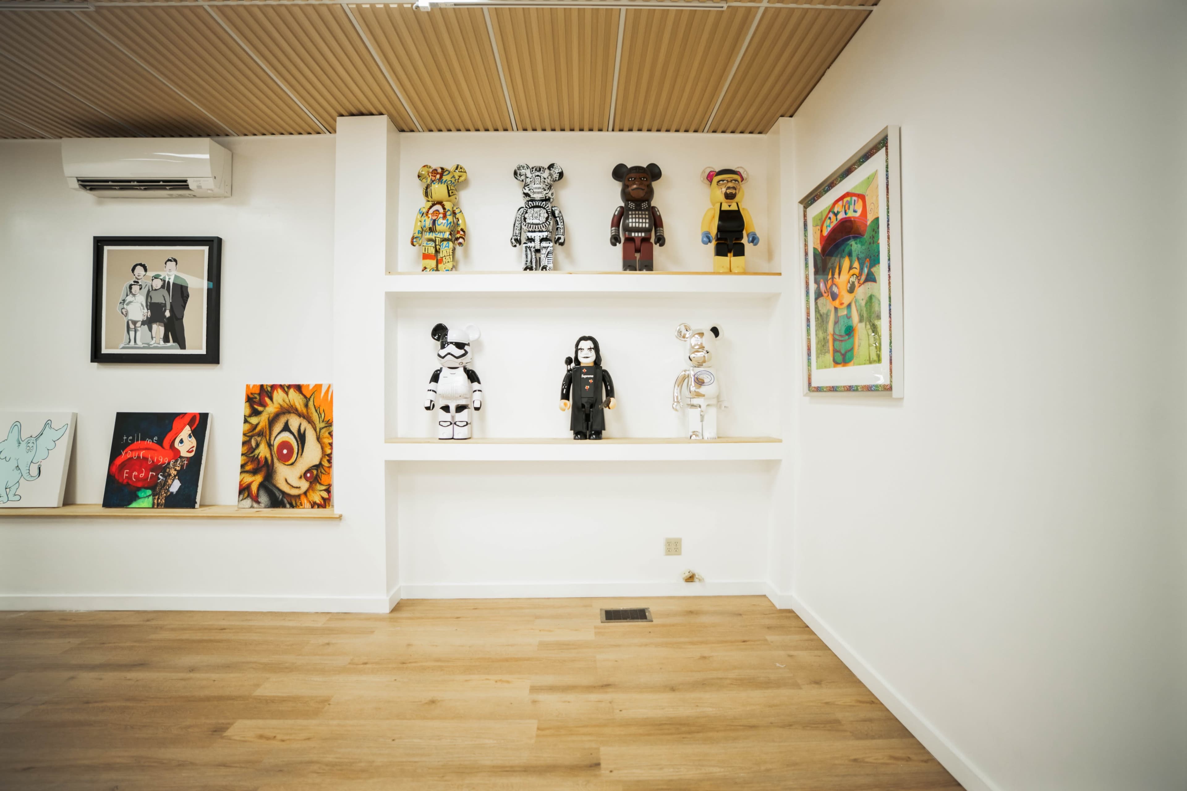 A white wall with a shelf displaying various artistic figurines, alongside framed artworks and photographs.