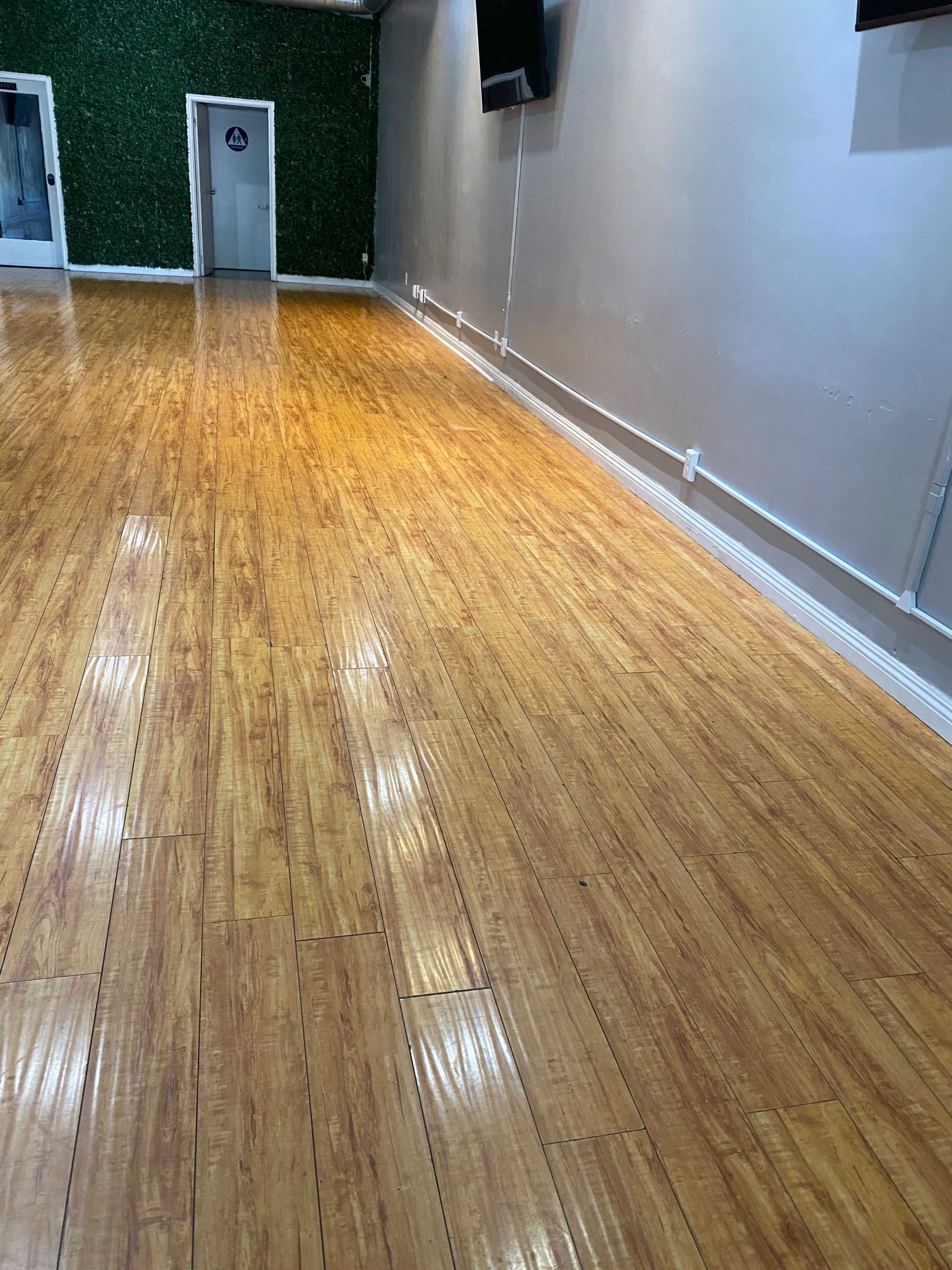 The image shows a spacious room with polished wooden floors and green wall decor at one end.