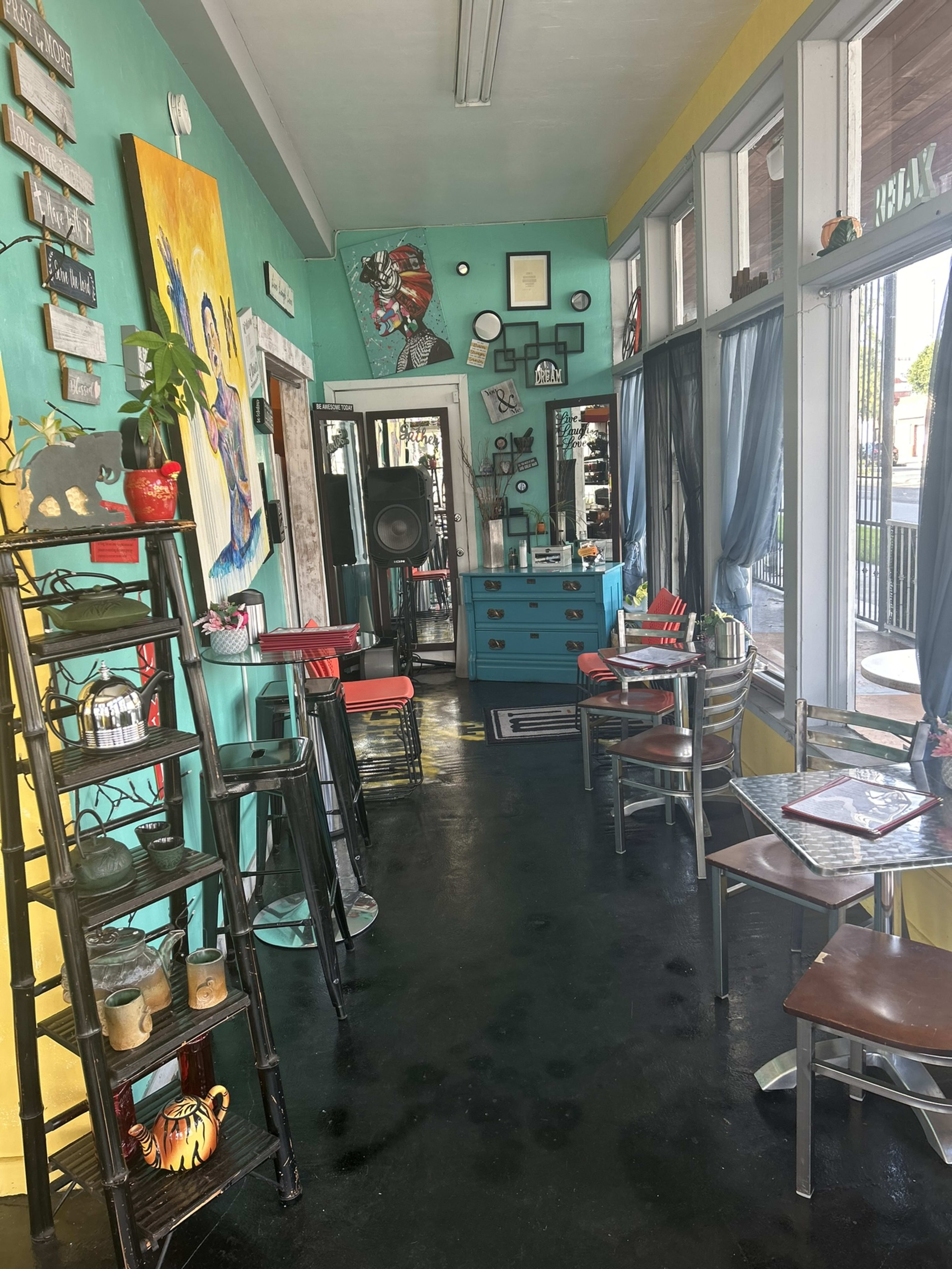 A colorful cafe interior featuring teal walls, wooden furniture, and decorative art pieces.