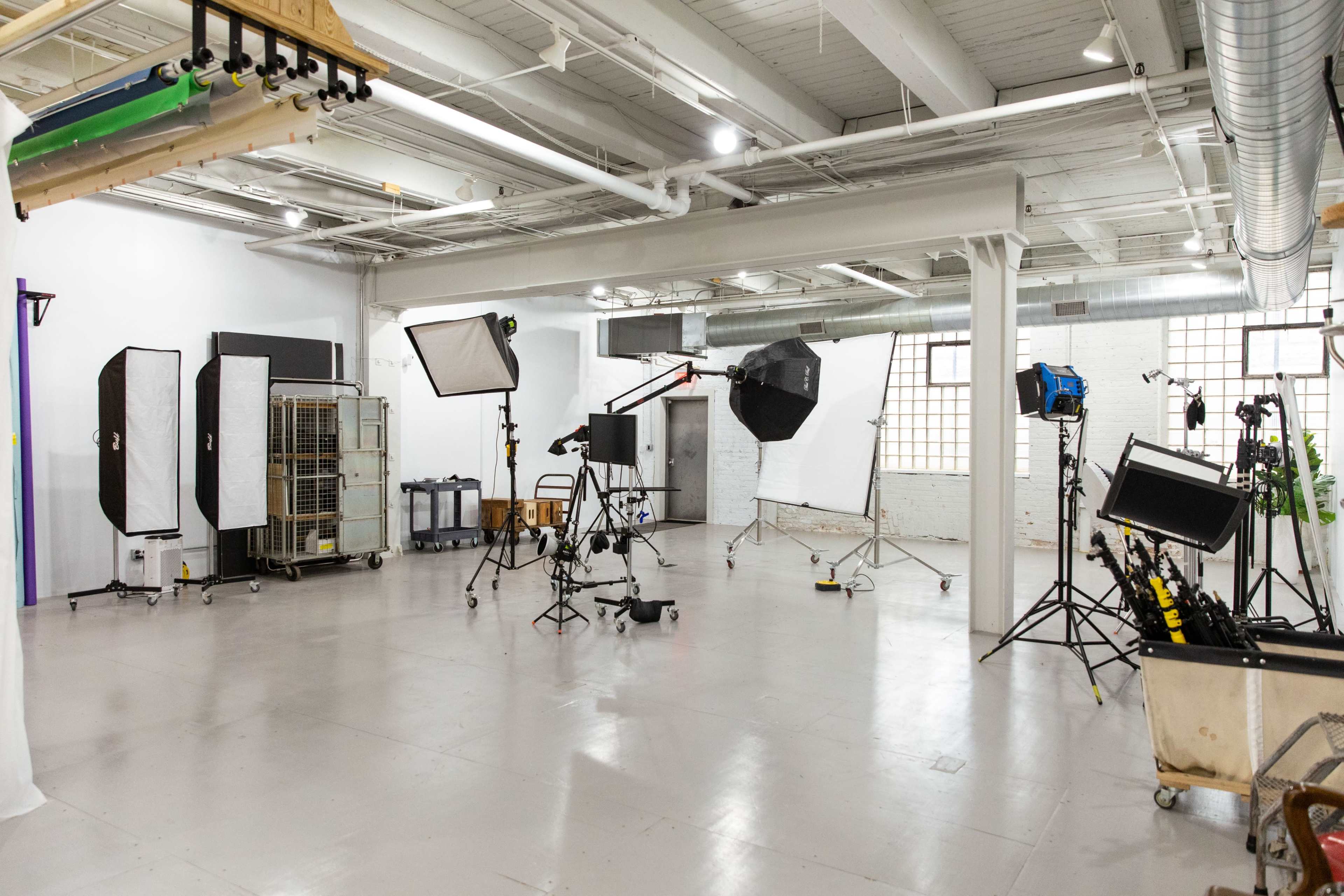 The image shows a photography studio equipped with various lighting setups and backdrops.