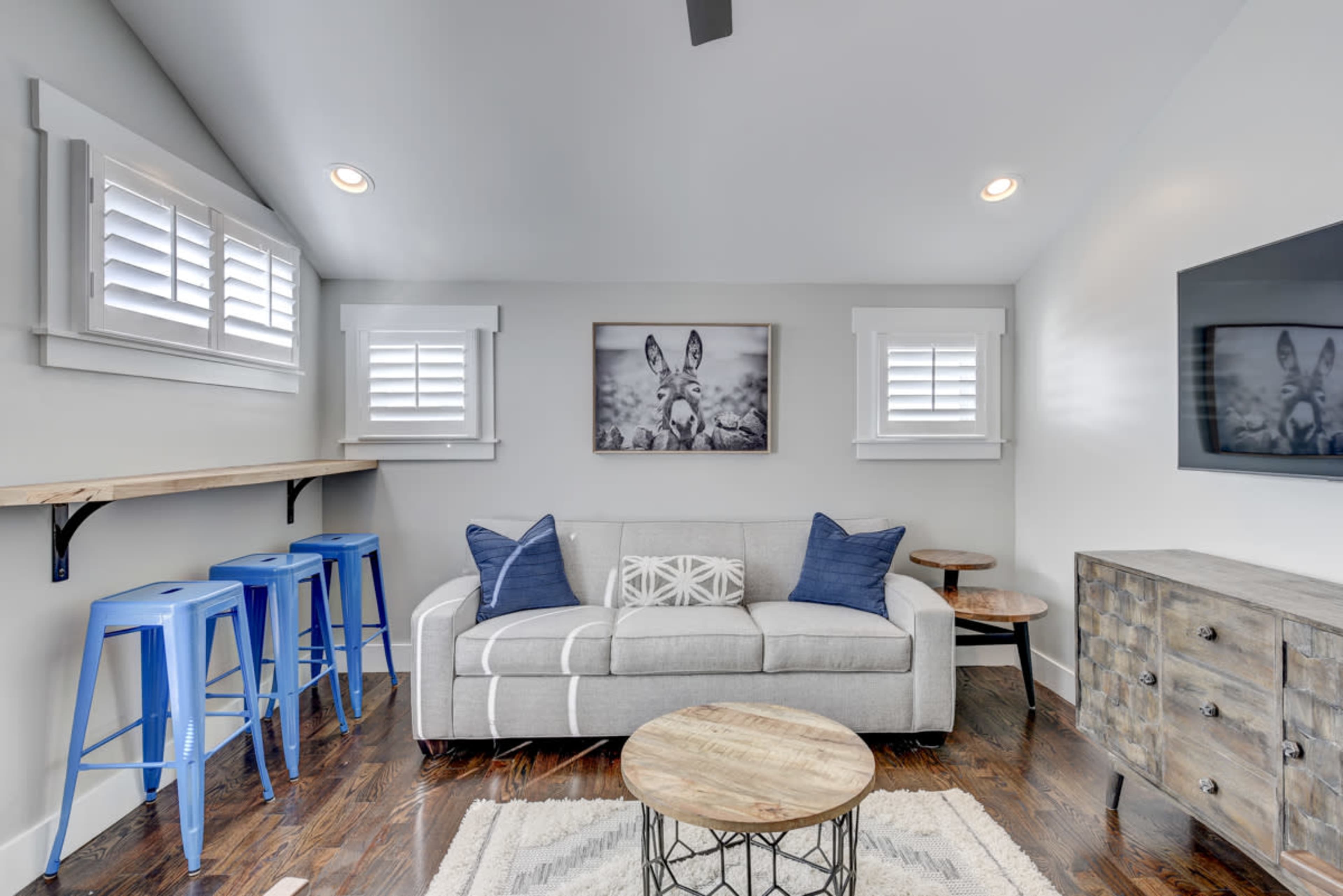 A modern living room with a gray sofa, blue bar stools, a wooden coffee table, and a wall-mounted television.