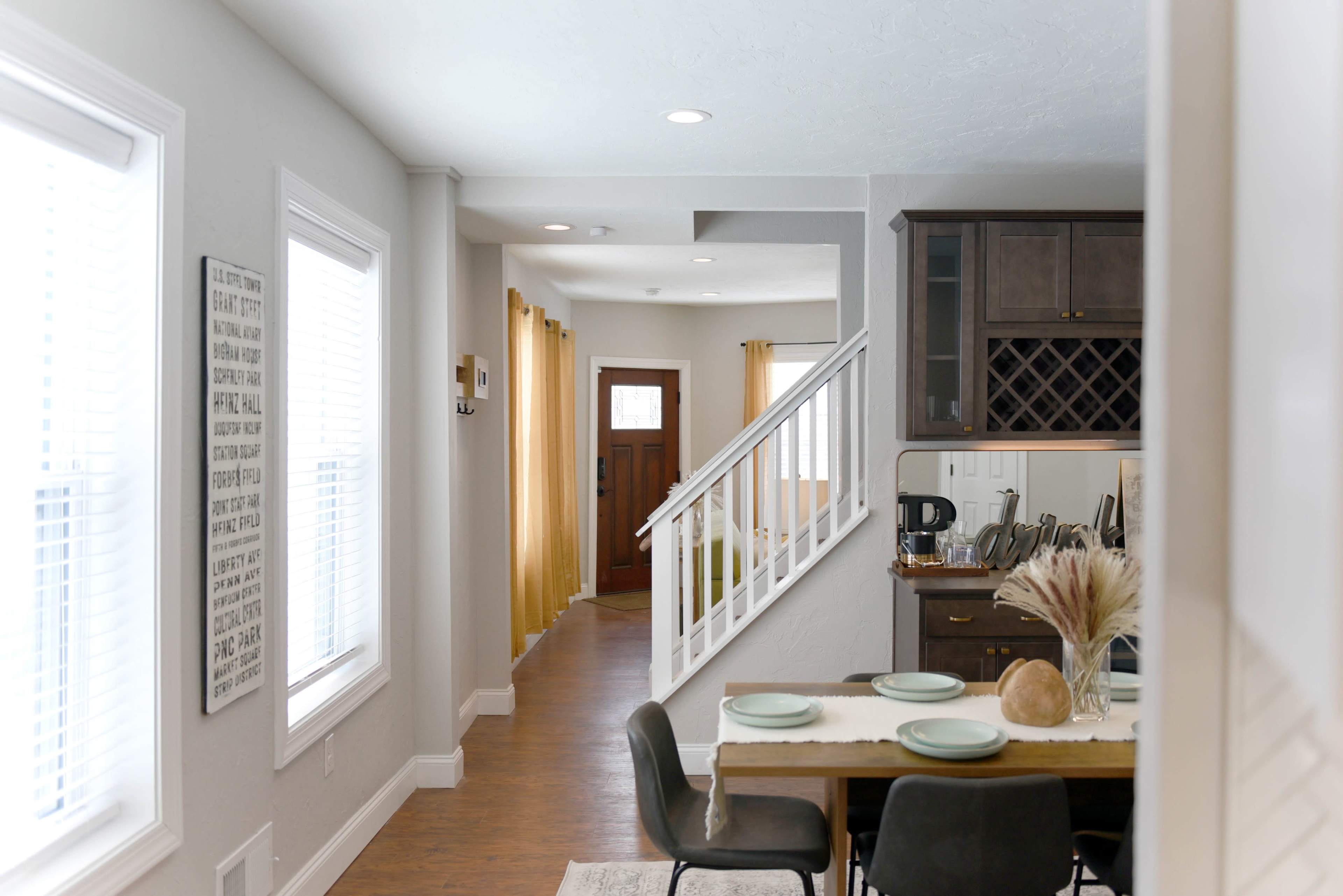 A clean, modern interior of a home with a dining area in the foreground, a staircase leading to the upper floor, and a doorway visible in the background.