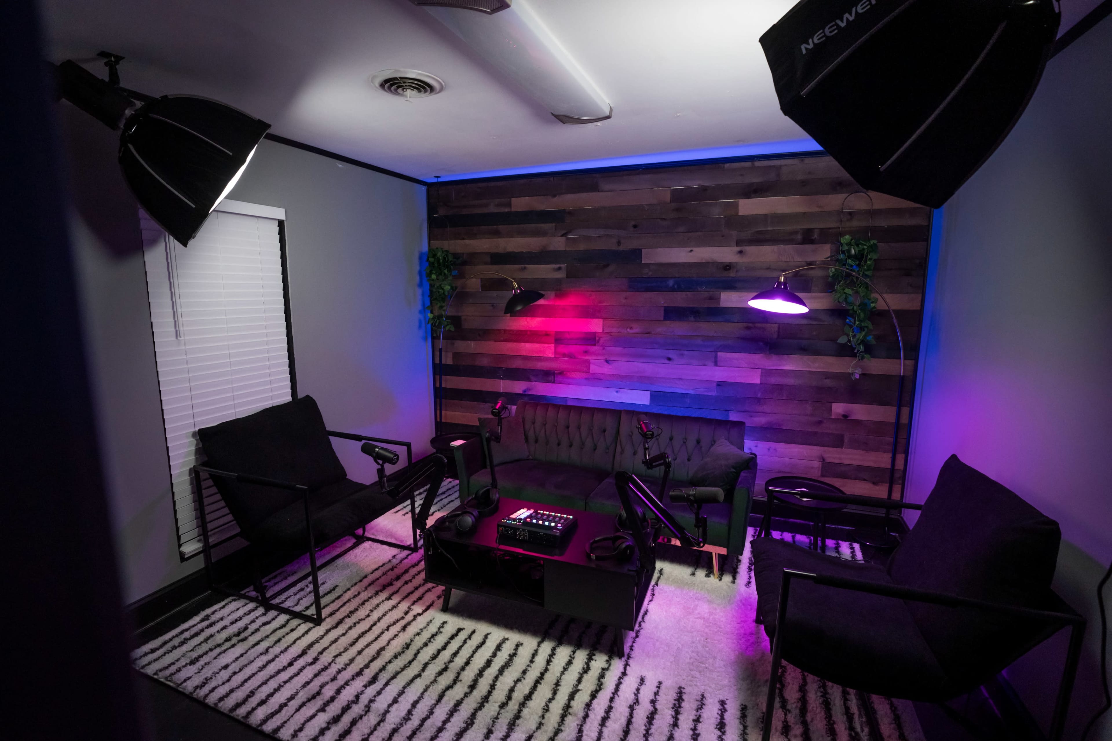 A modern lounge area features a black couch and chairs, a dark coffee table, and lighting against a wooden accent wall.