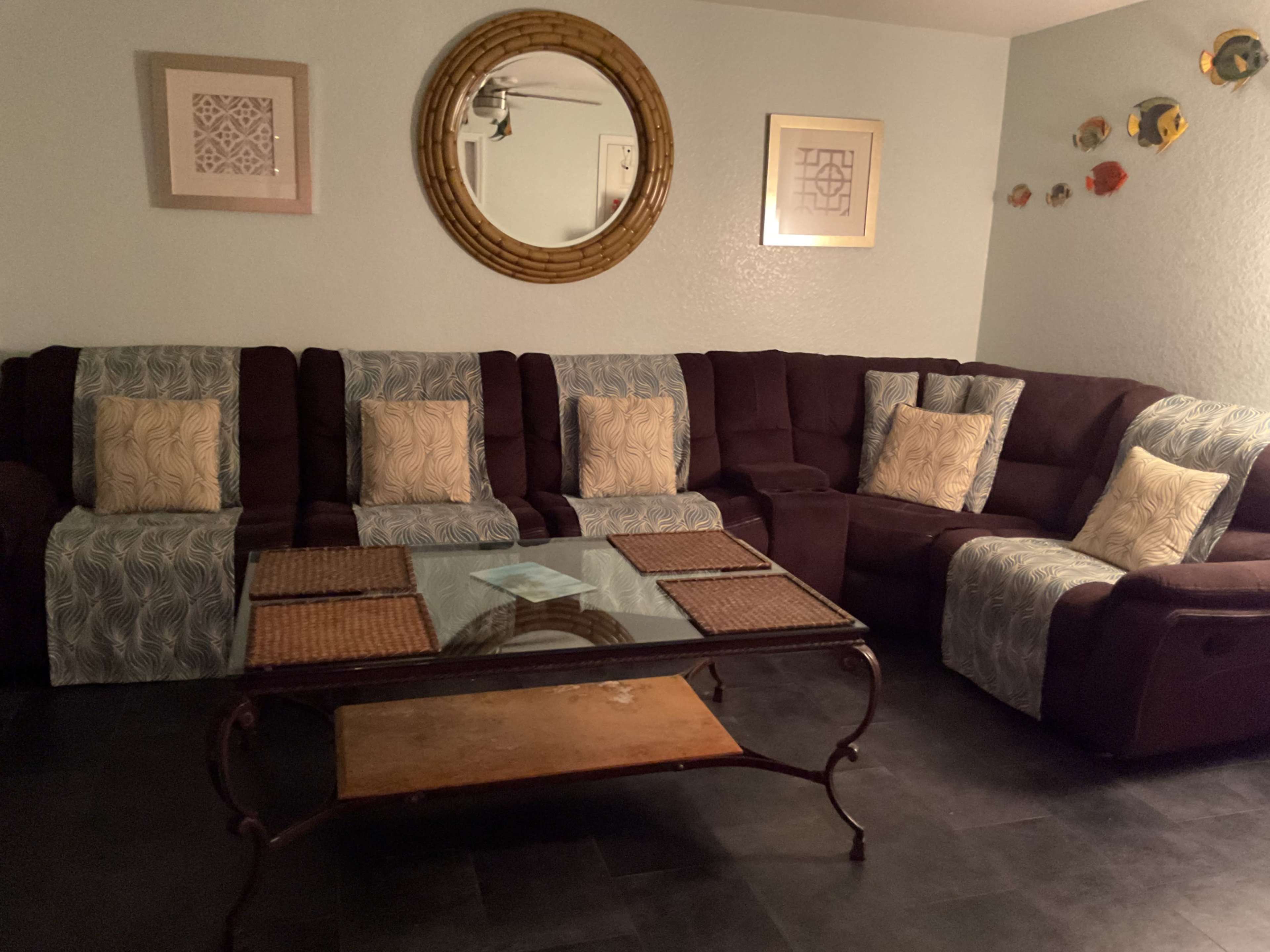 The image shows a living room with a large sectional couch, a glass coffee table, and decorative wall art.