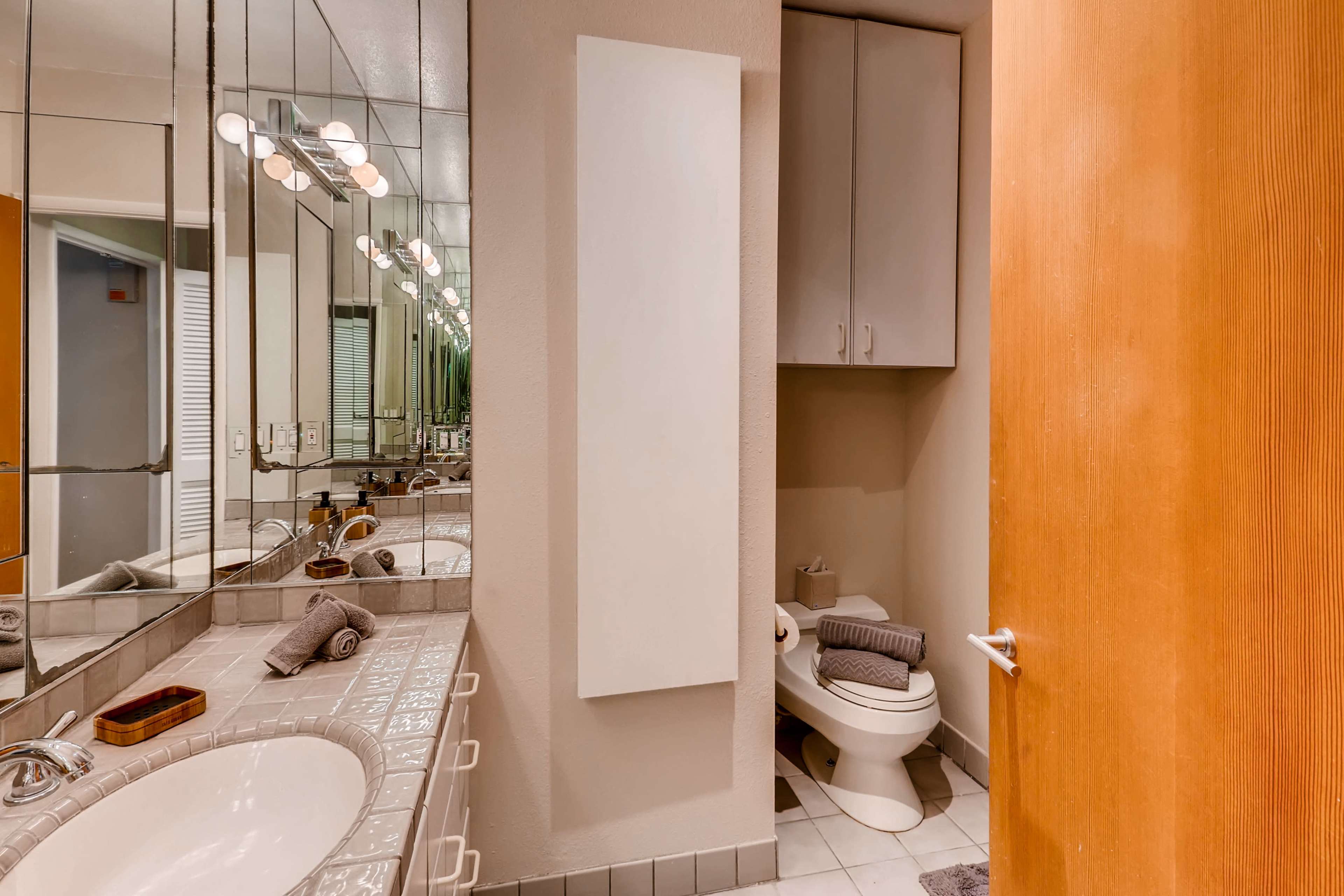 A bathroom with a vanity area, a mirror, a toilet, and a wooden door.