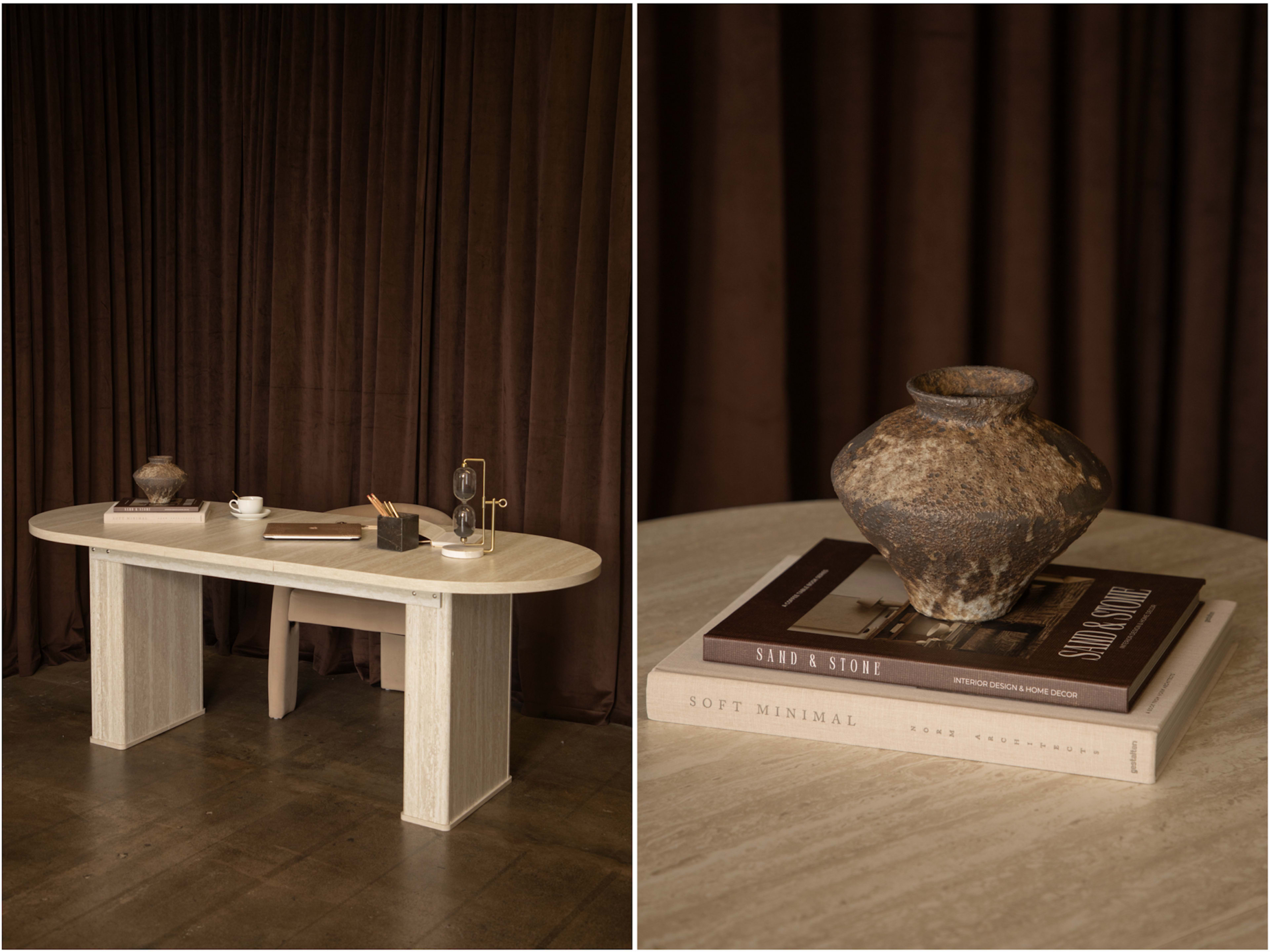 A minimalistic wooden table is set against a draped brown backdrop, with a decorative vase and stacked books positioned on top.