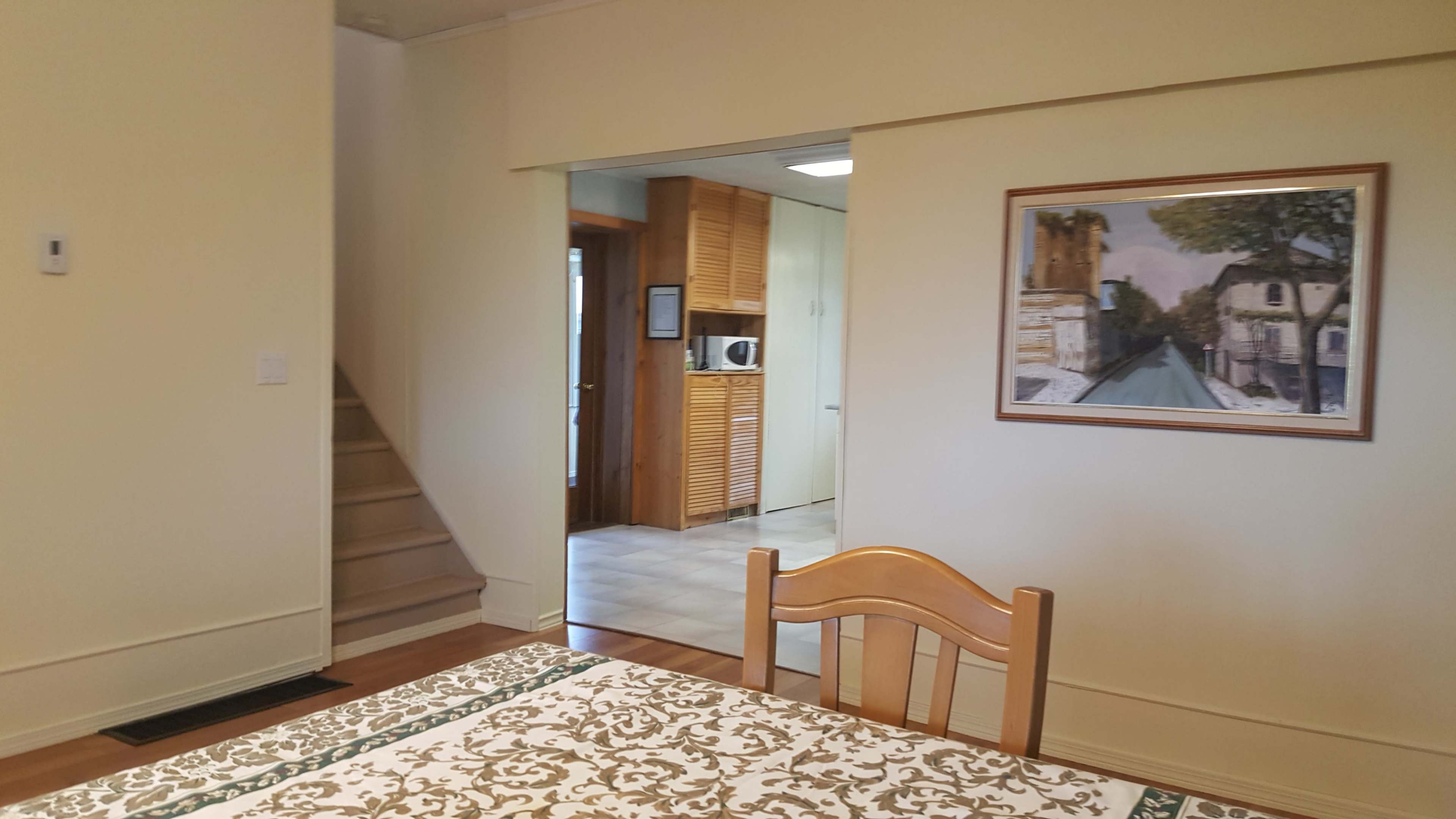 A dining table with a patterned tablecloth is positioned in a room that opens to a staircase and a kitchen area.
