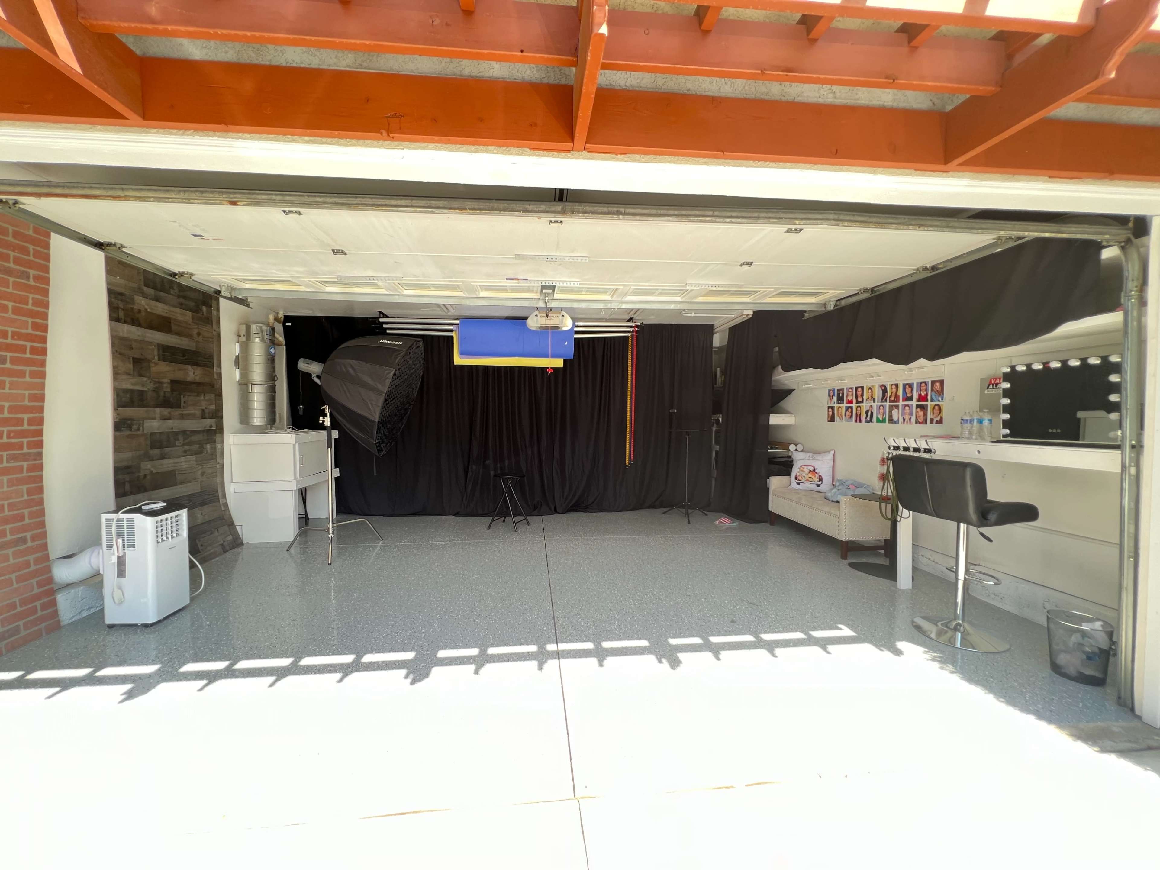 A garage is converted into a photography studio with a black backdrop, lighting equipment, and a seating area.