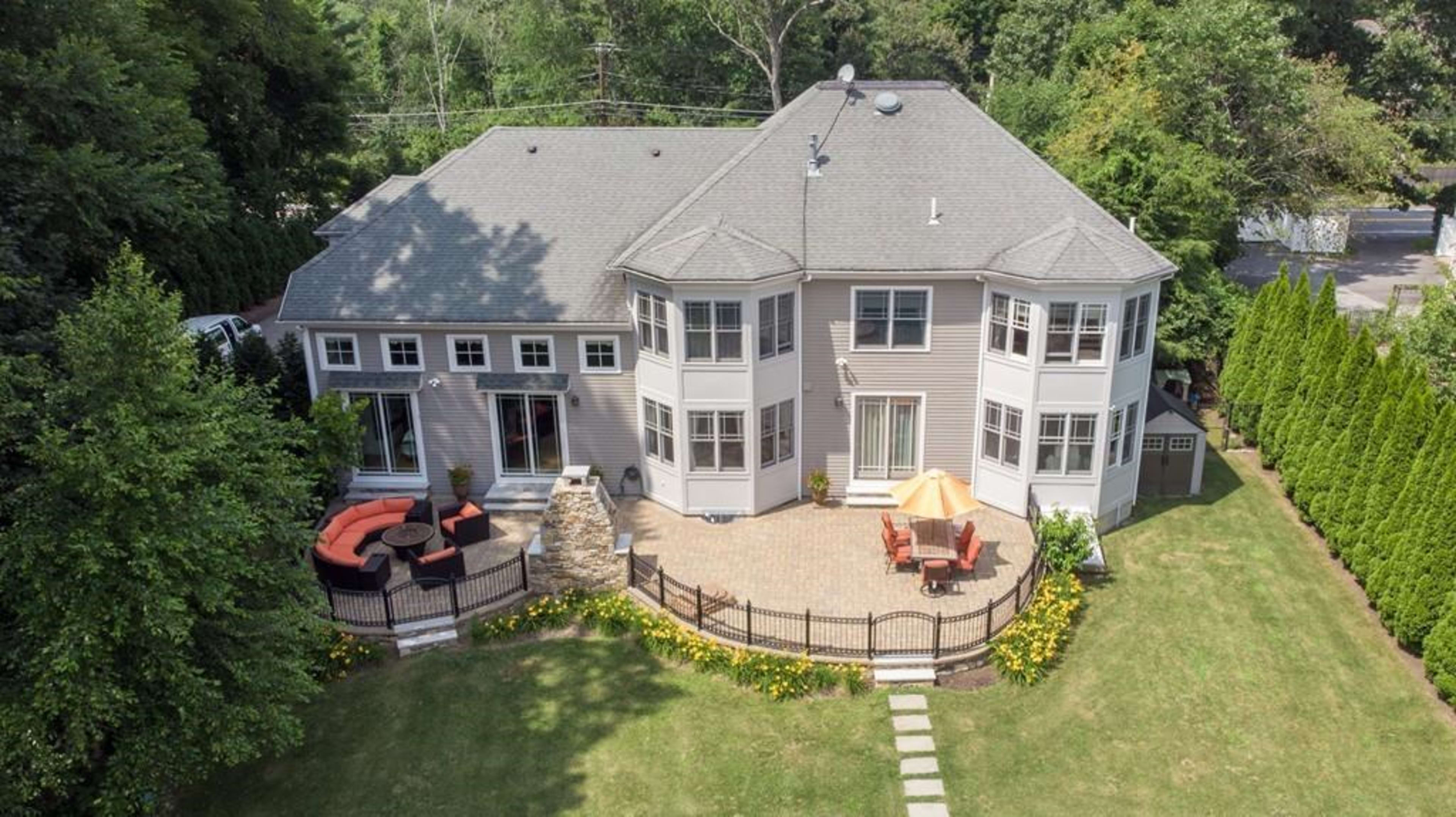 A spacious, modern house with multiple windows and a landscaped yard featuring a stone patio and outdoor seating.