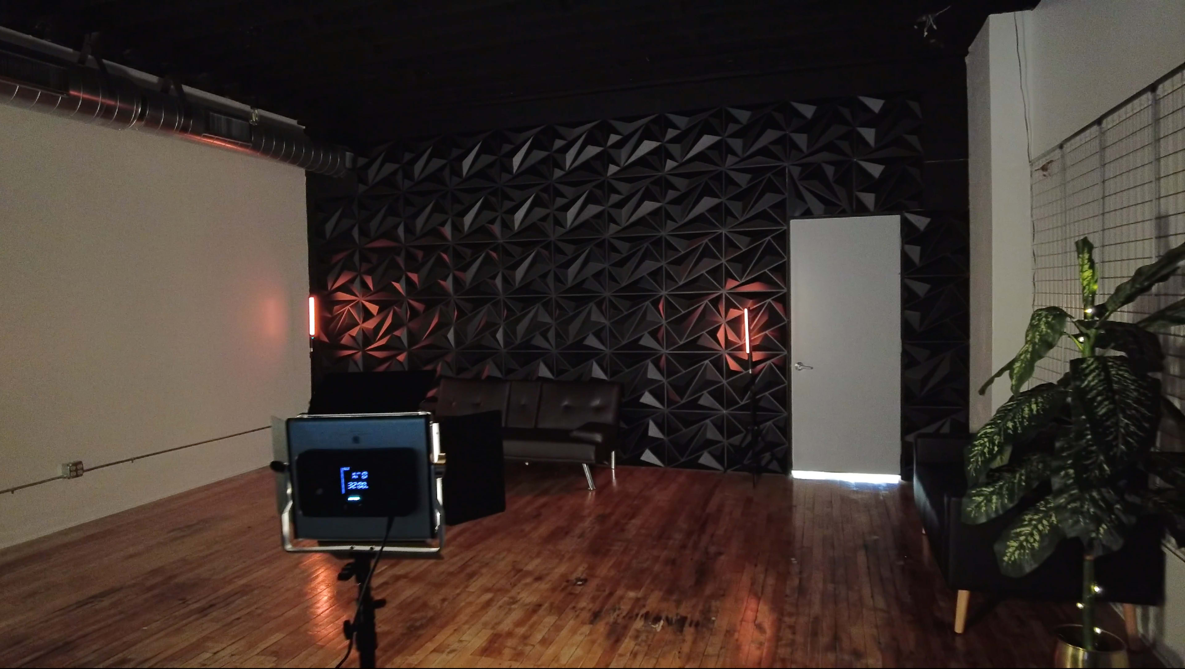 An empty room with a textured black wall, a sofa, and a door partially open to reveal light.