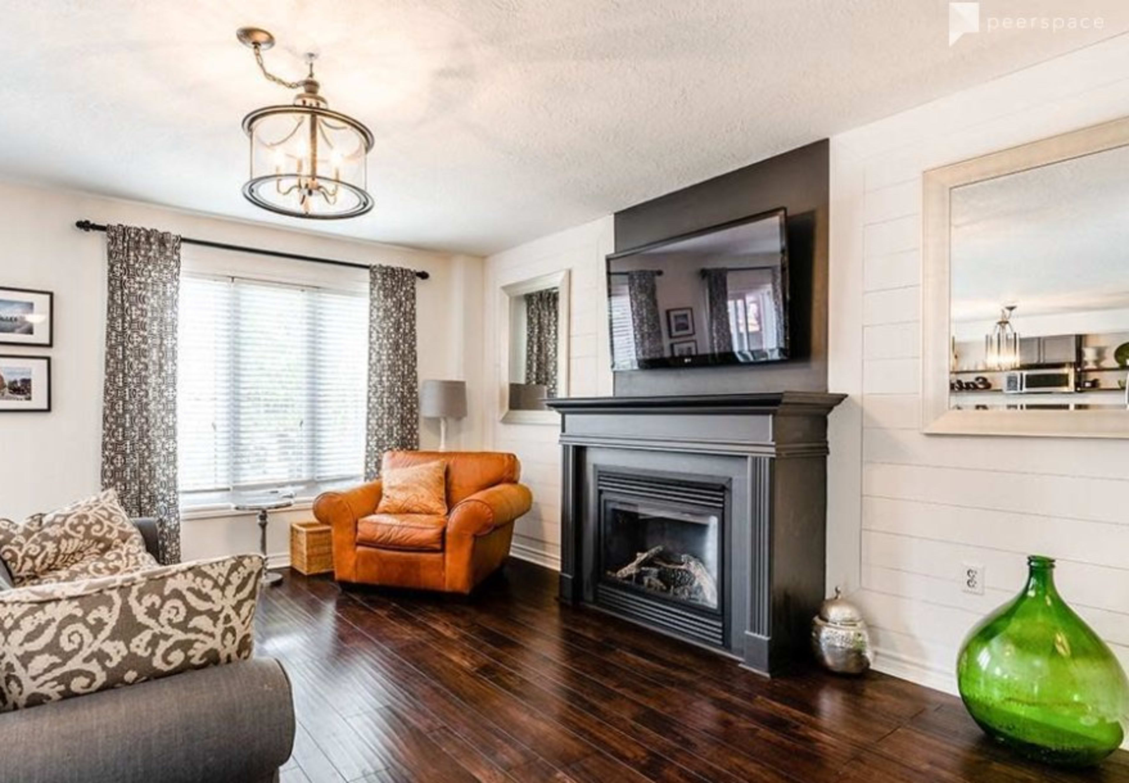 A cozy living room with a brown leather armchair, a black fireplace, a television mounted on a wall, and hardwood floors.