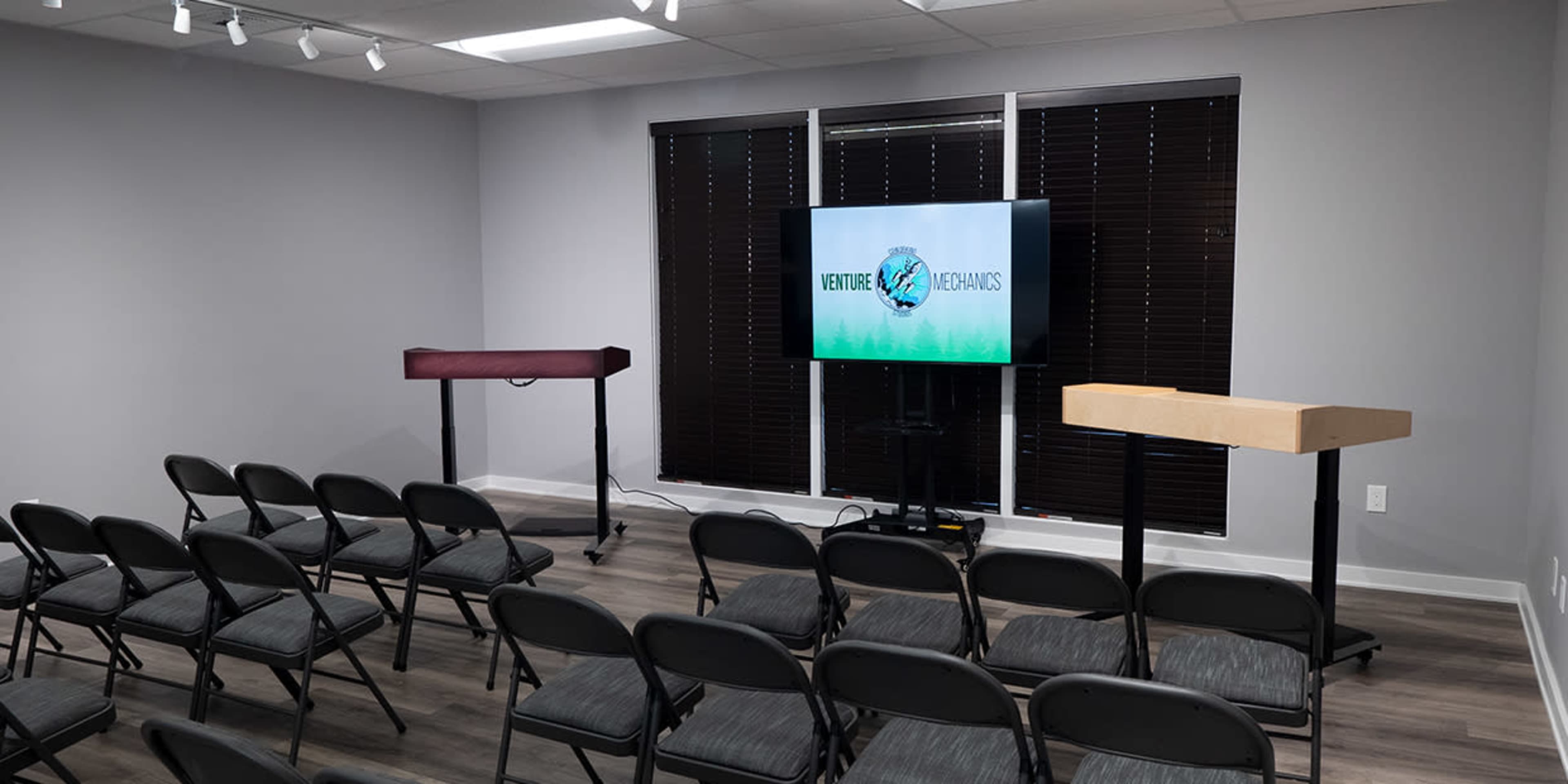A conference room set up with black folding chairs facing two podiums and a large screen displaying the text "VENTURE METAMORPHOSIS."