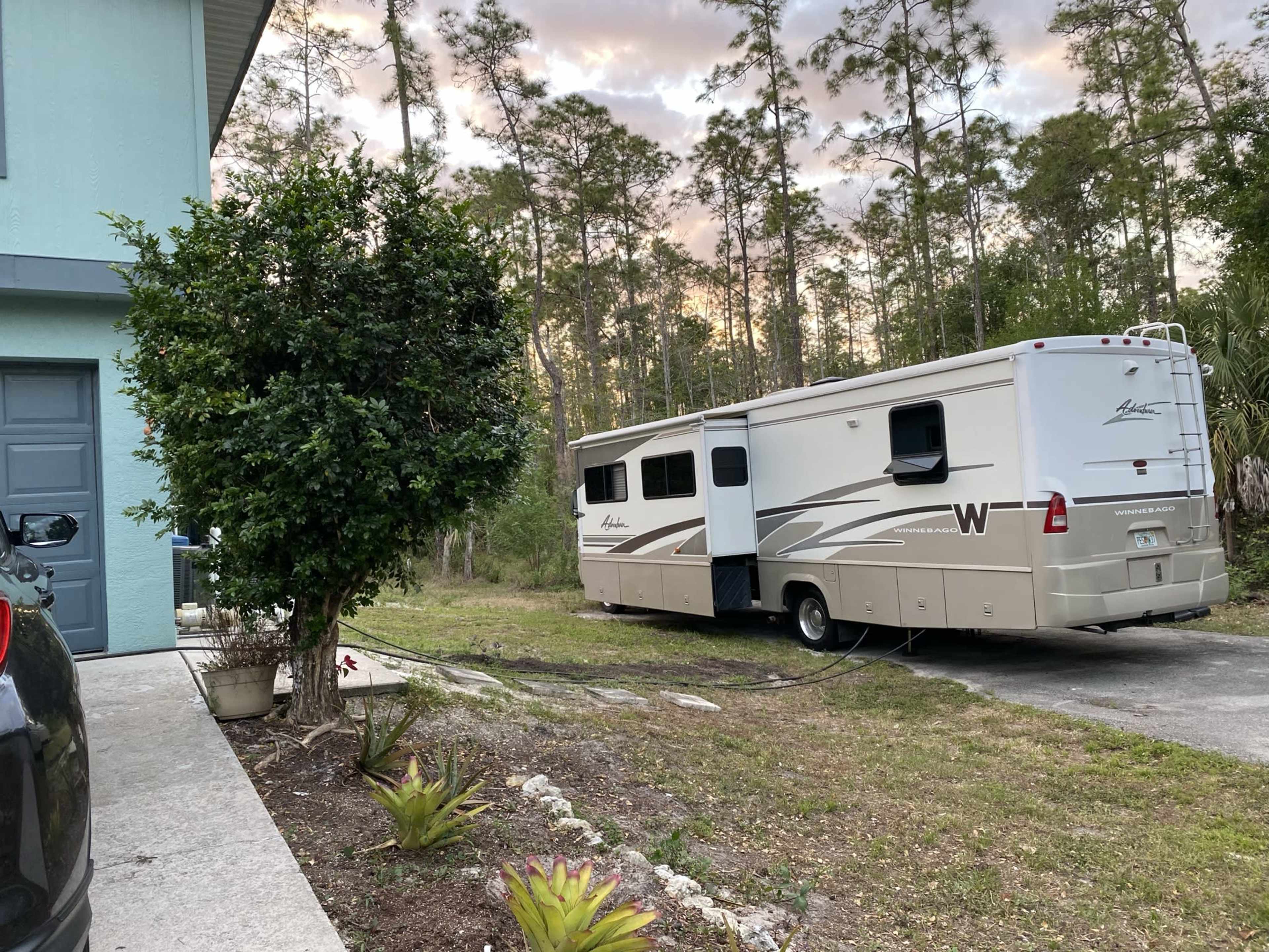 A recreational vehicle is parked beside a house in a grassy area surrounded by trees.