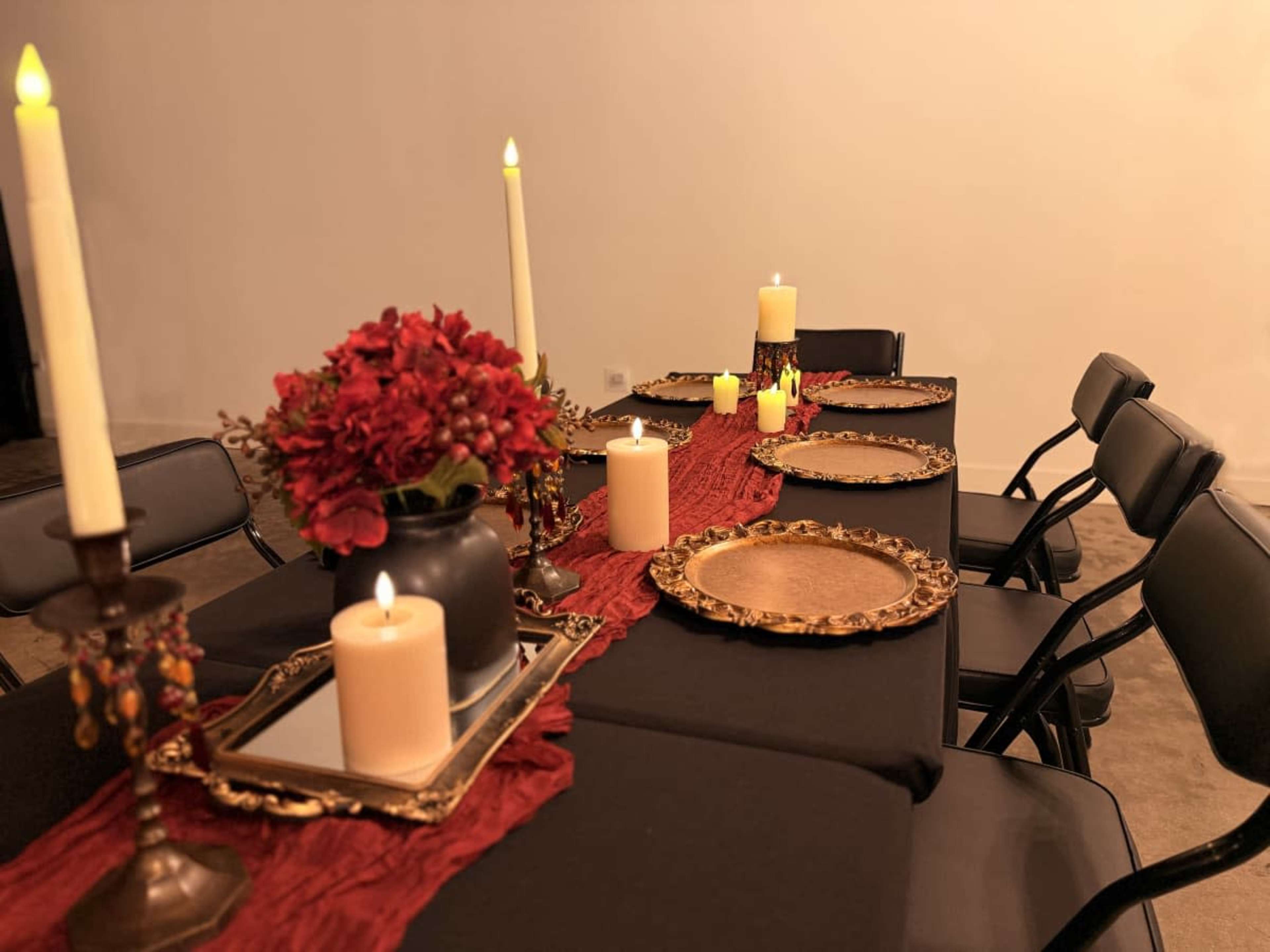 A dining table is set with black linens, gold and silver accents, floral centerpieces, and candles arranged along the center.