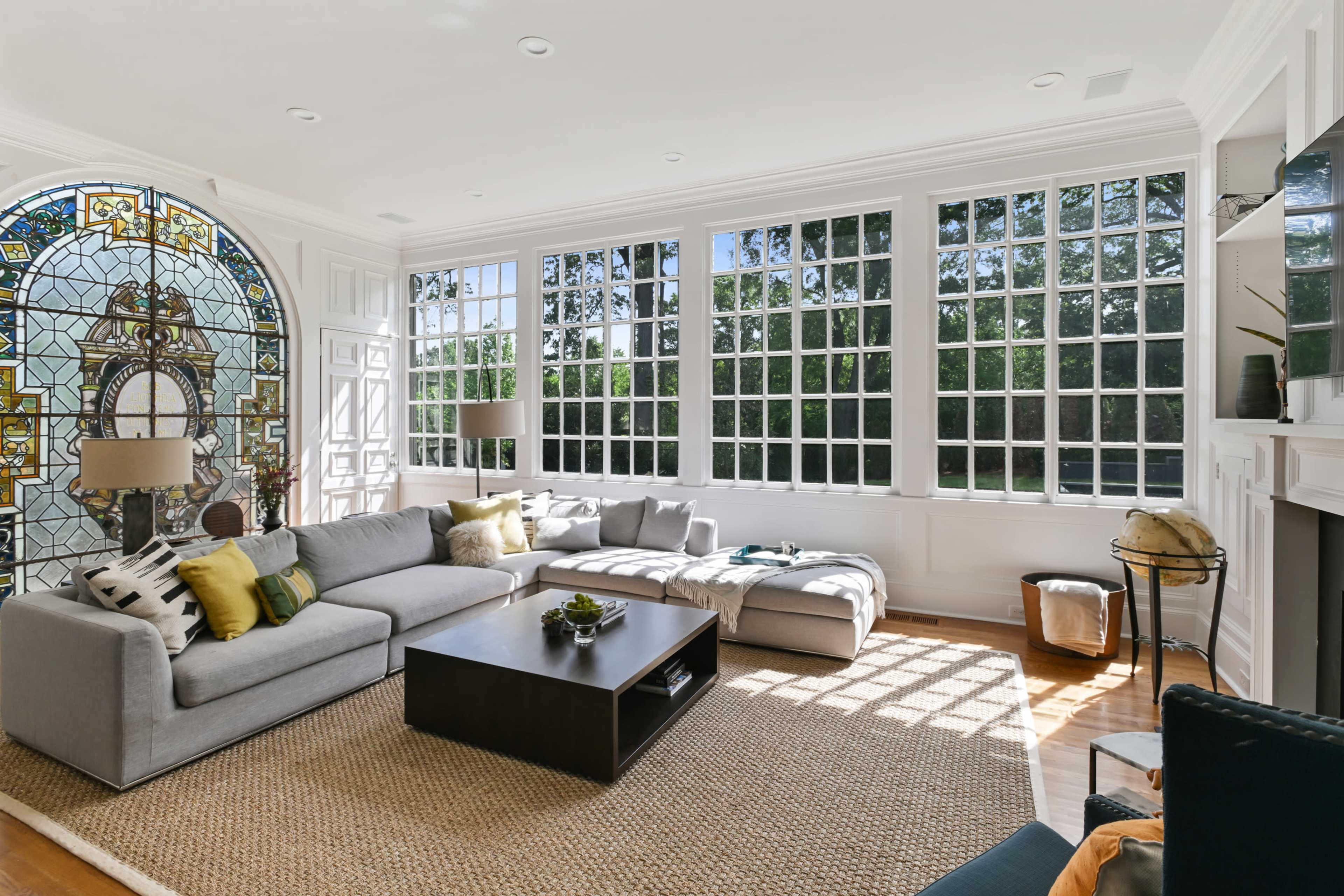 The living room features large windows that fill the space with natural light, a gray sectional sofa, and a coffee table on a textured rug.