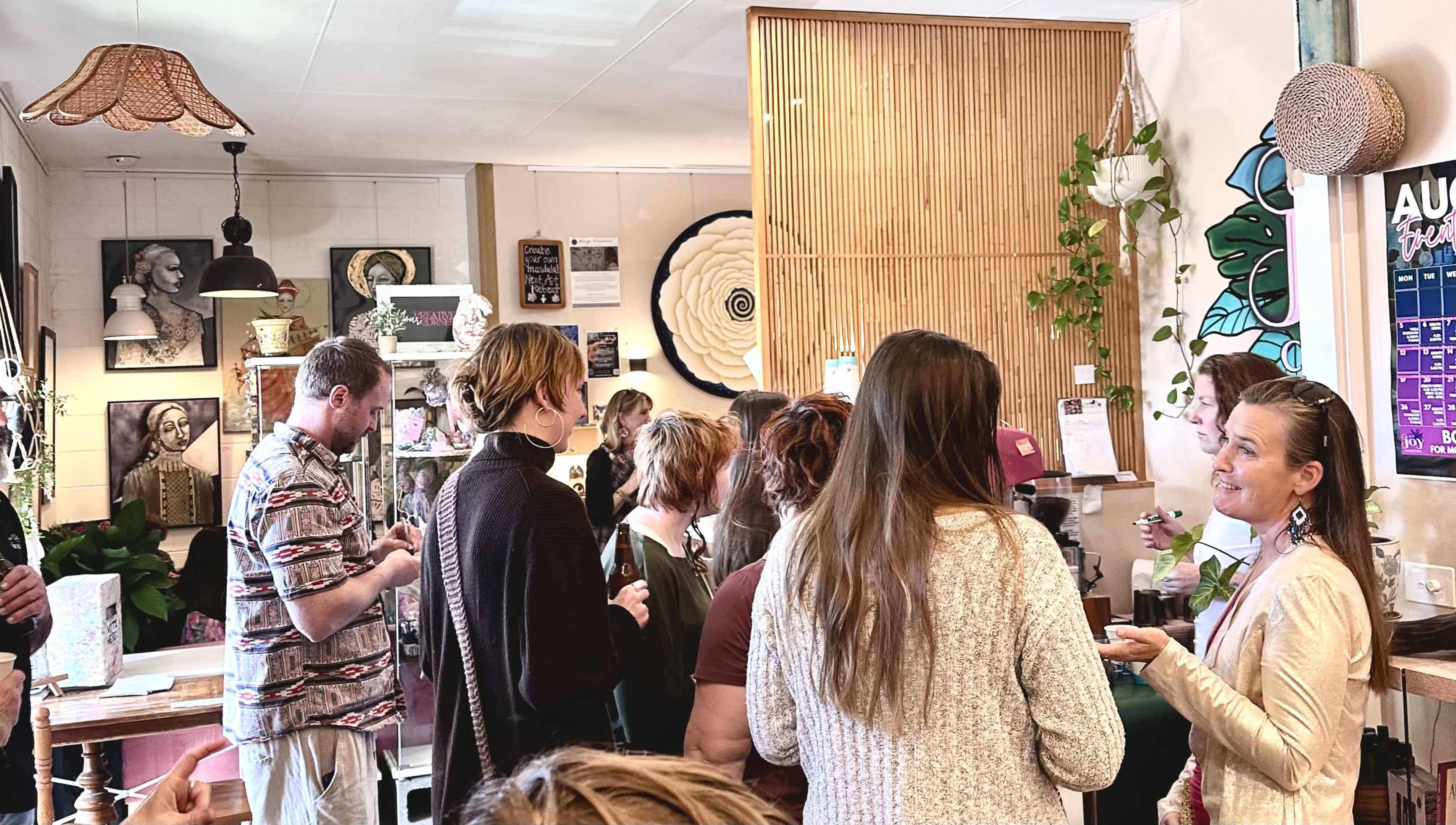 A group of people gathers in a cafe surrounded by various artworks and decor, engaging in conversation while some are at the service counter.
