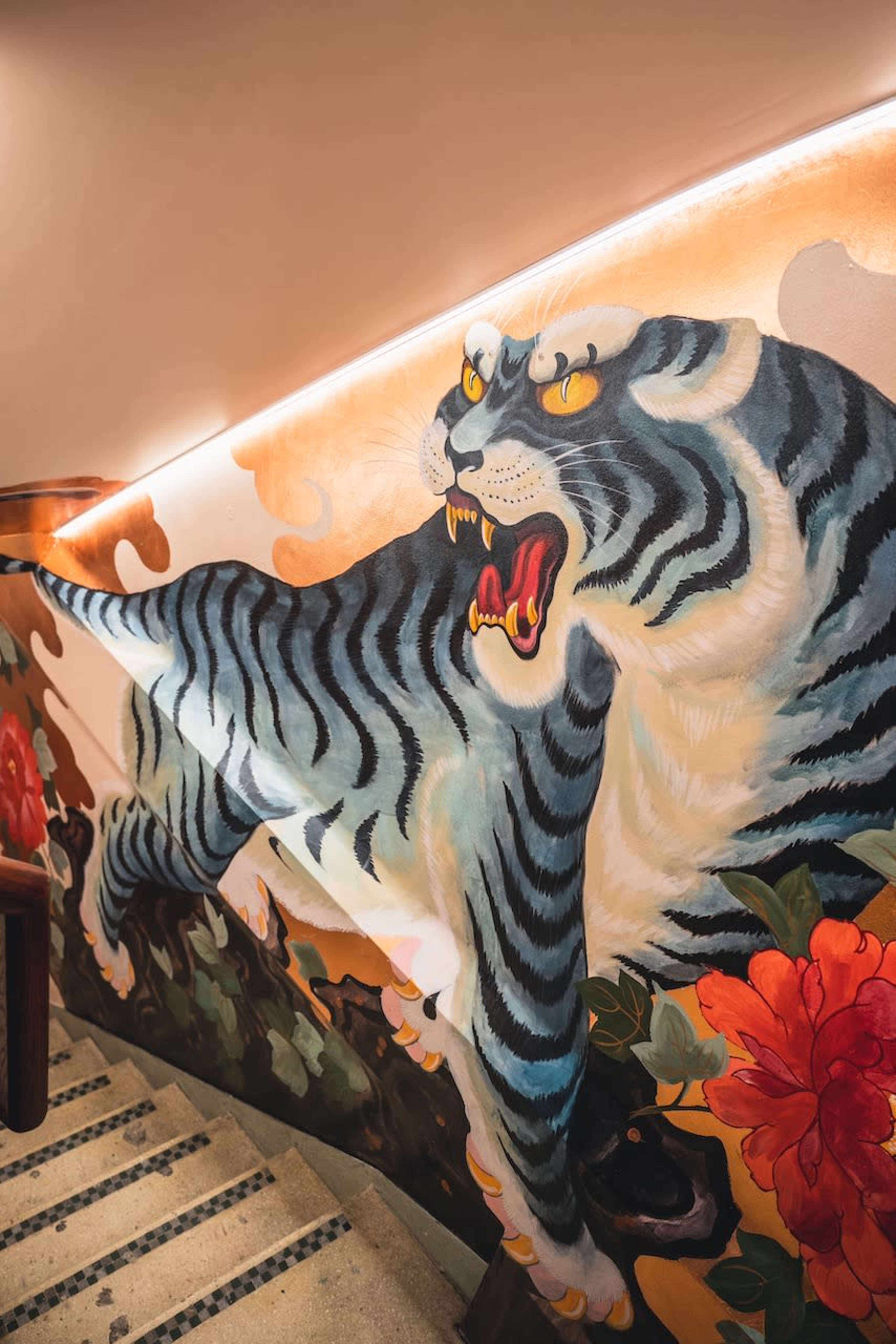 A large, colorful mural of a tiger is painted on the wall above a staircase, with floral designs surrounding it.