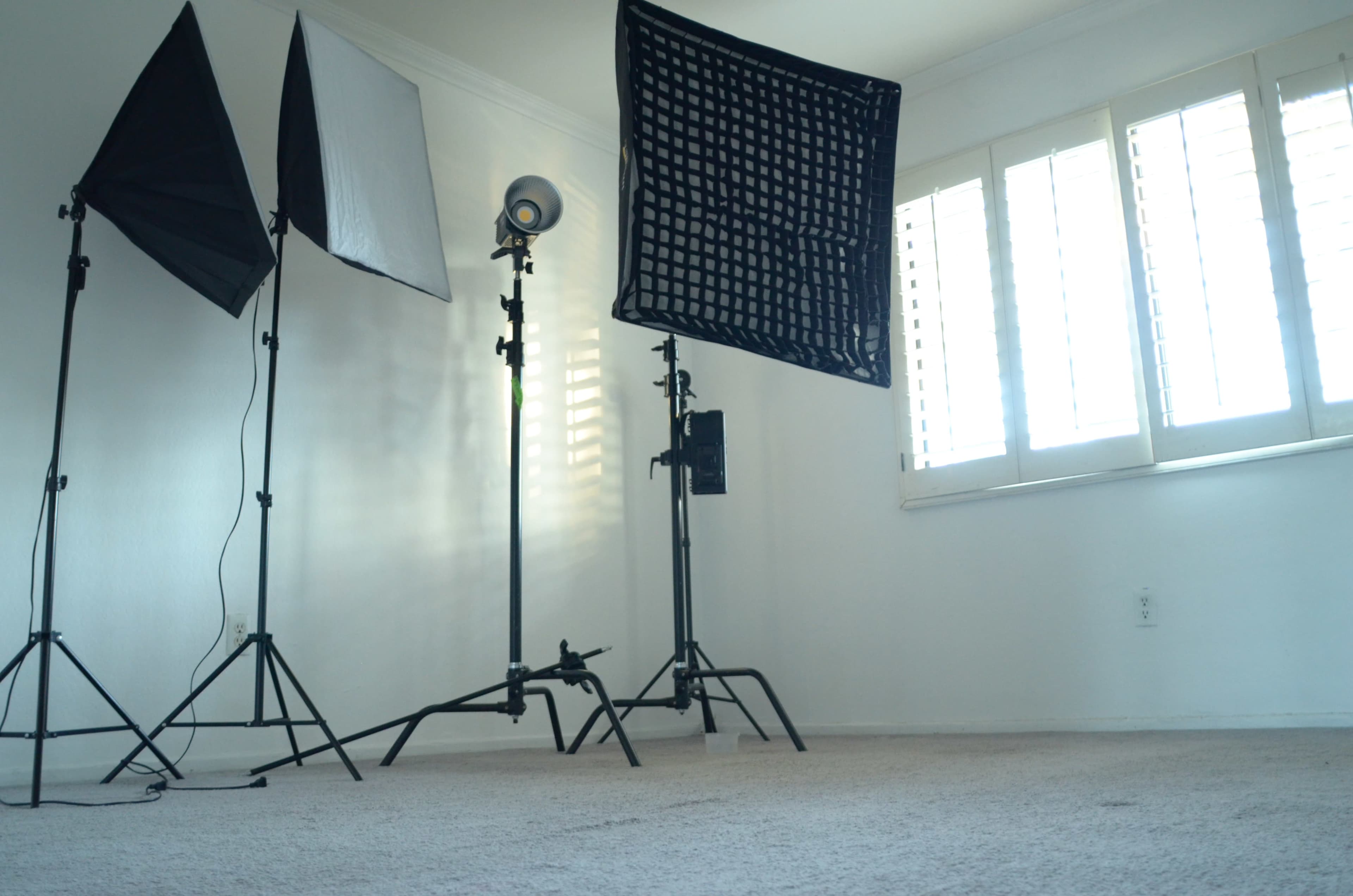 A photography setup with three light stands and softboxes in an empty room with shuttered windows.