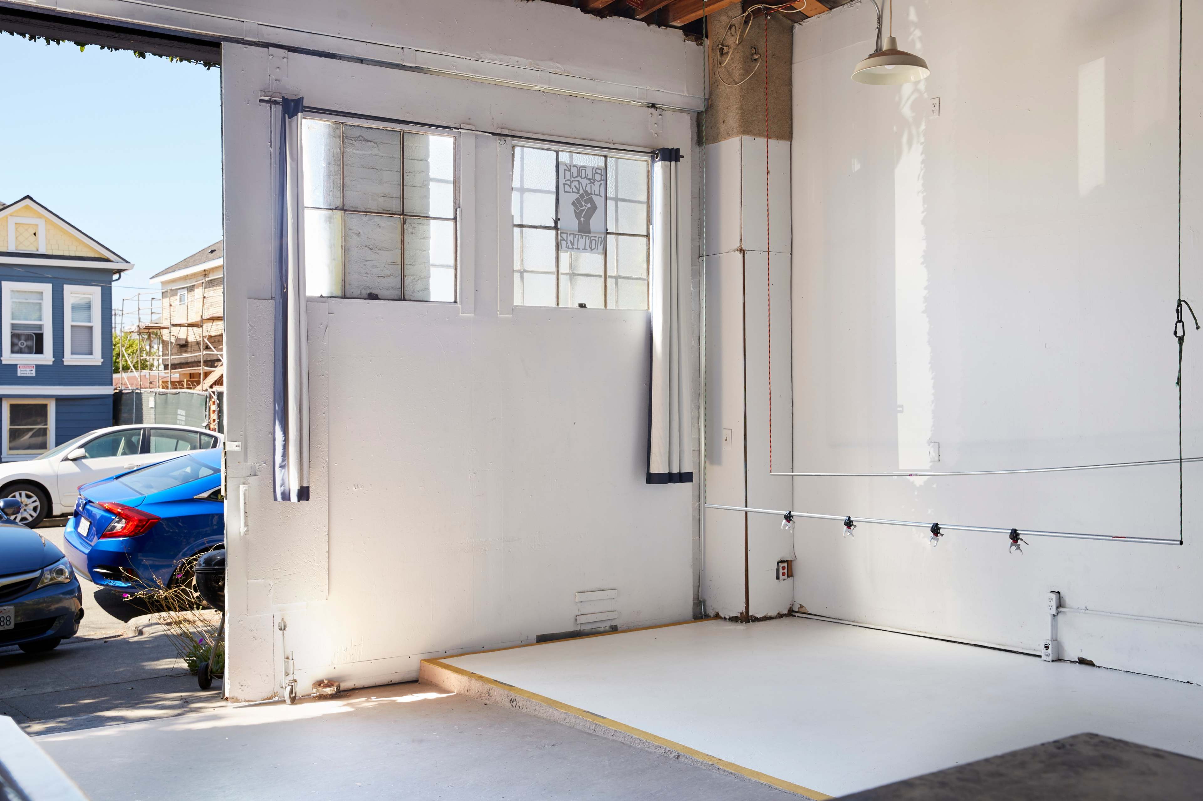 A spacious room with a white floor and large windows, revealing an exterior view of parked cars and a building.