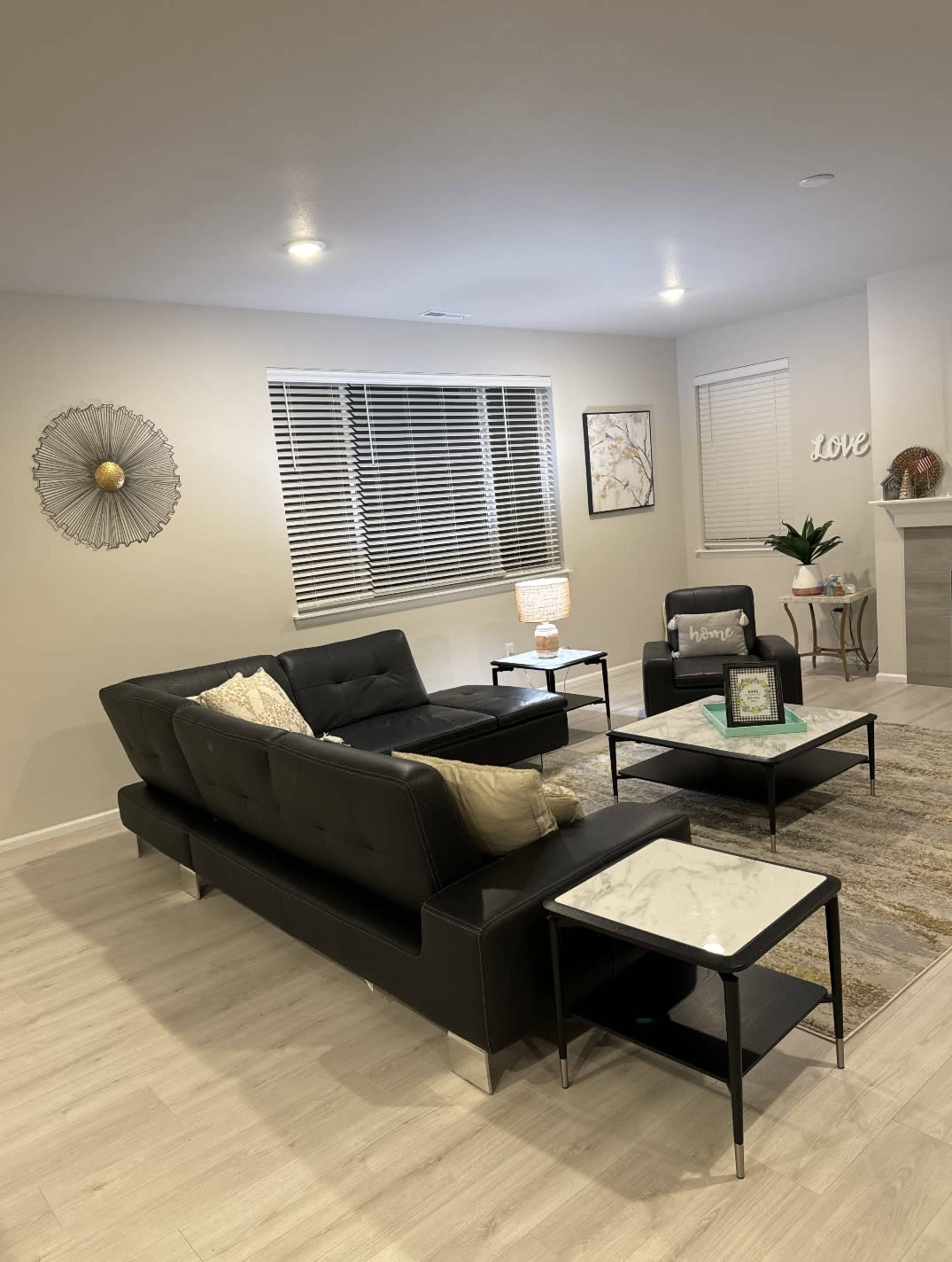 A modern living room features a black leather sofa, two black chairs, and marble-top coffee tables, with decorative wall art and a lamp illuminating the space.