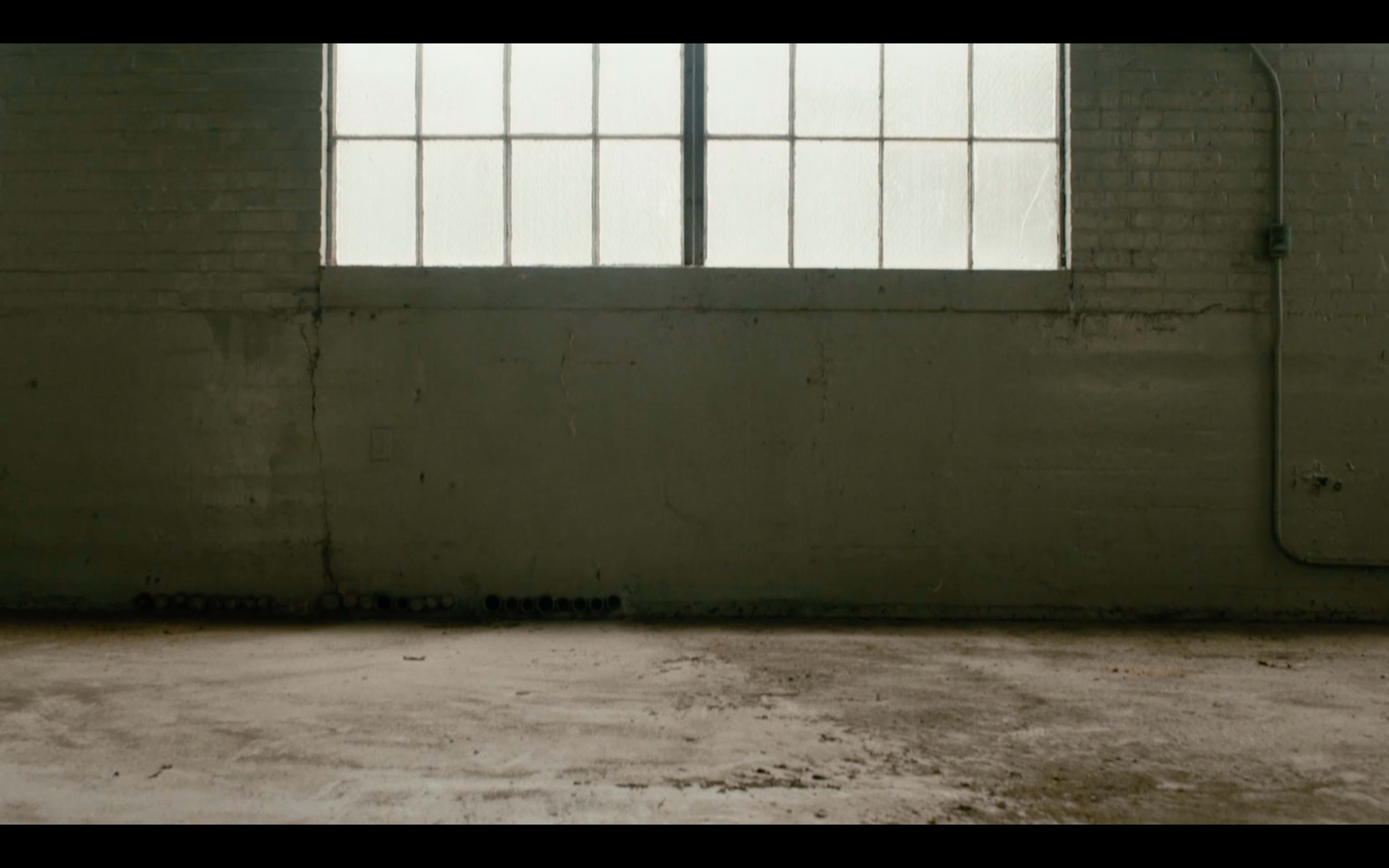 An empty room features a concrete floor and a large window with multiple panes allowing diffused light to enter.