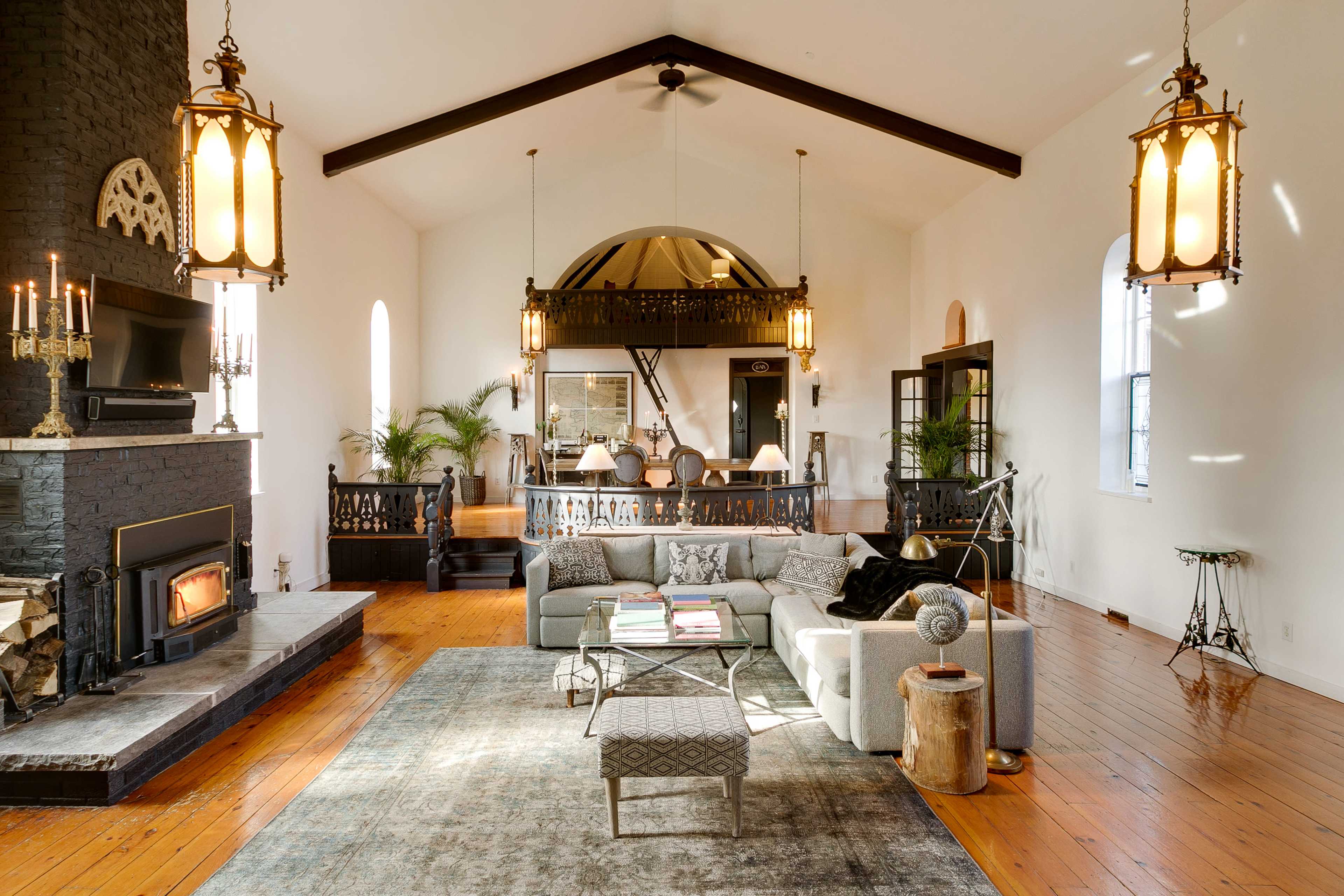 A spacious living room features high ceilings, large windows, a fireplace, and a mix of modern and traditional furnishings.