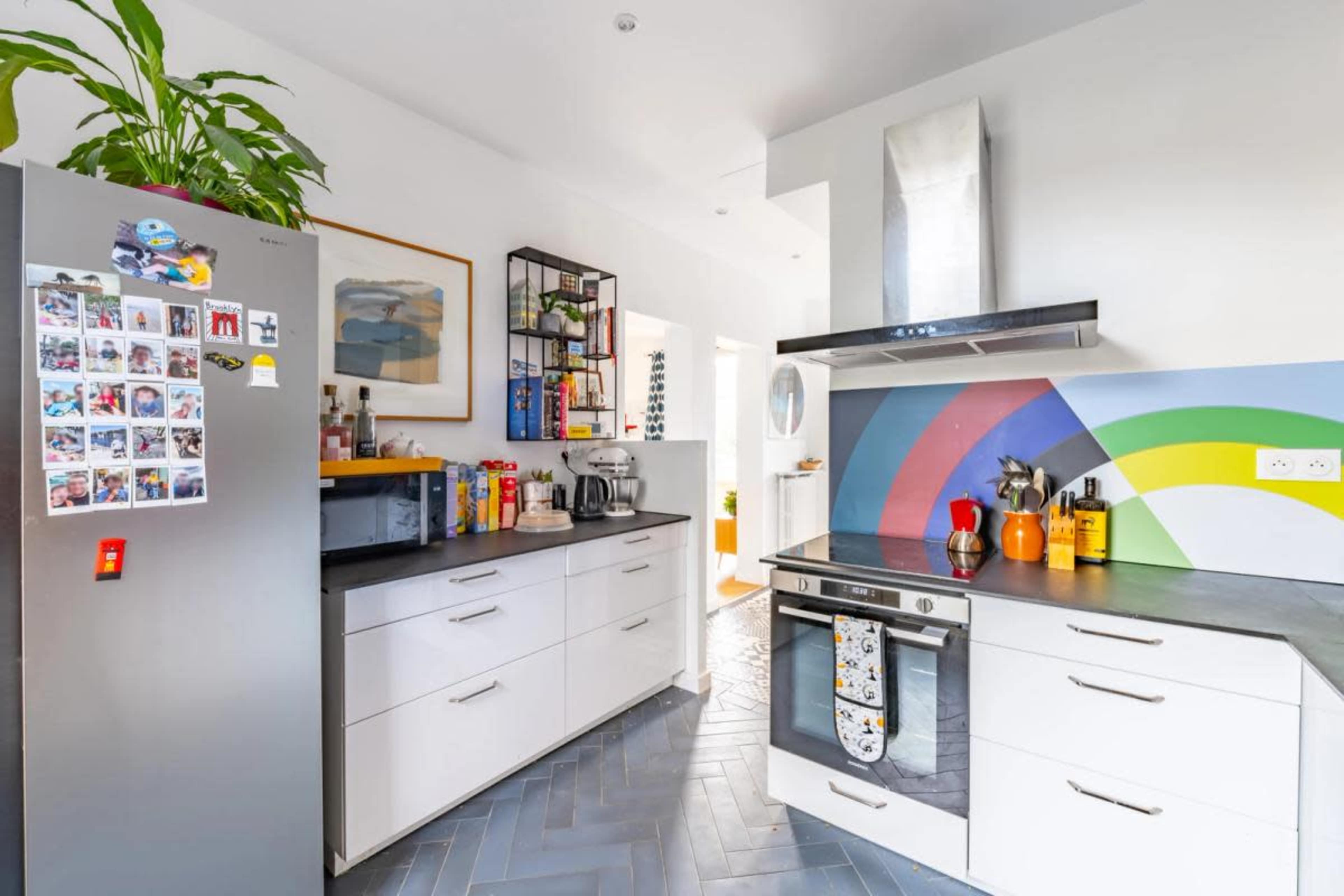 A modern kitchen with white cabinetry, a colorful backsplash, stainless steel appliances, and a vibrant decorative element on the wall.