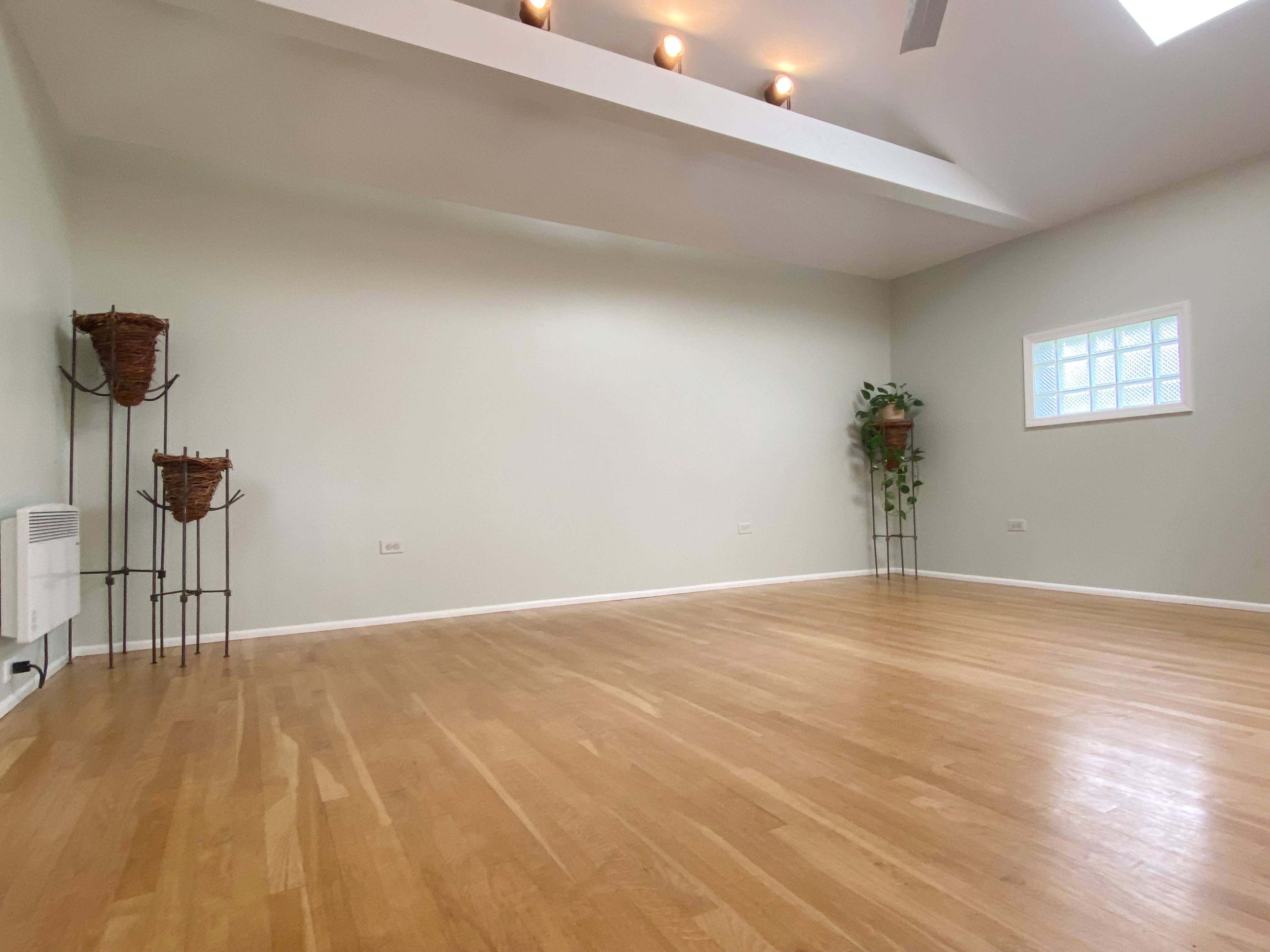 A spacious room with wooden floors, two decorative planters, and a small window near the ceiling.