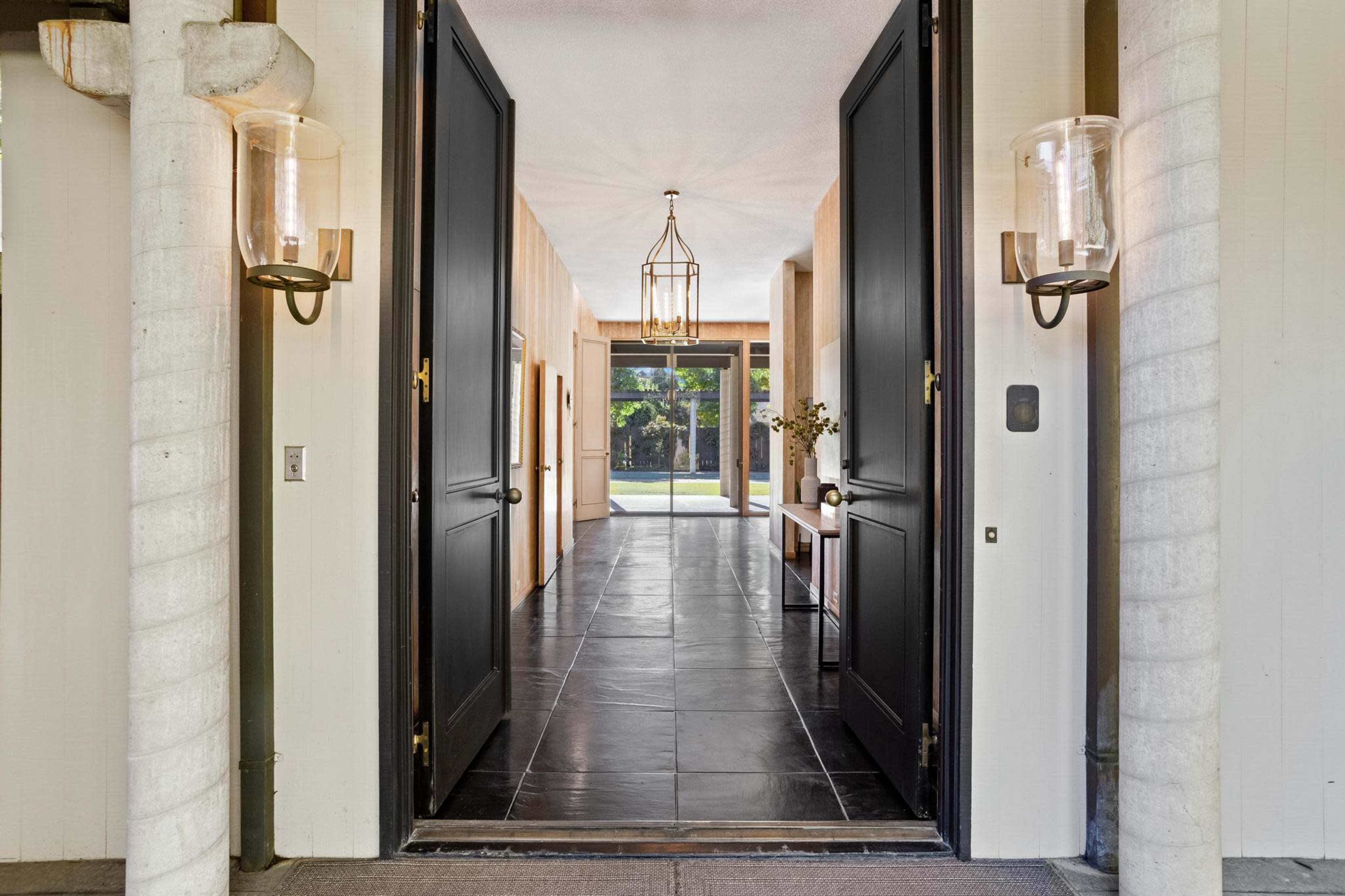 A spacious entryway with large black double doors opening into a long hallway lined with tiled flooring and modern lighting fixtures.