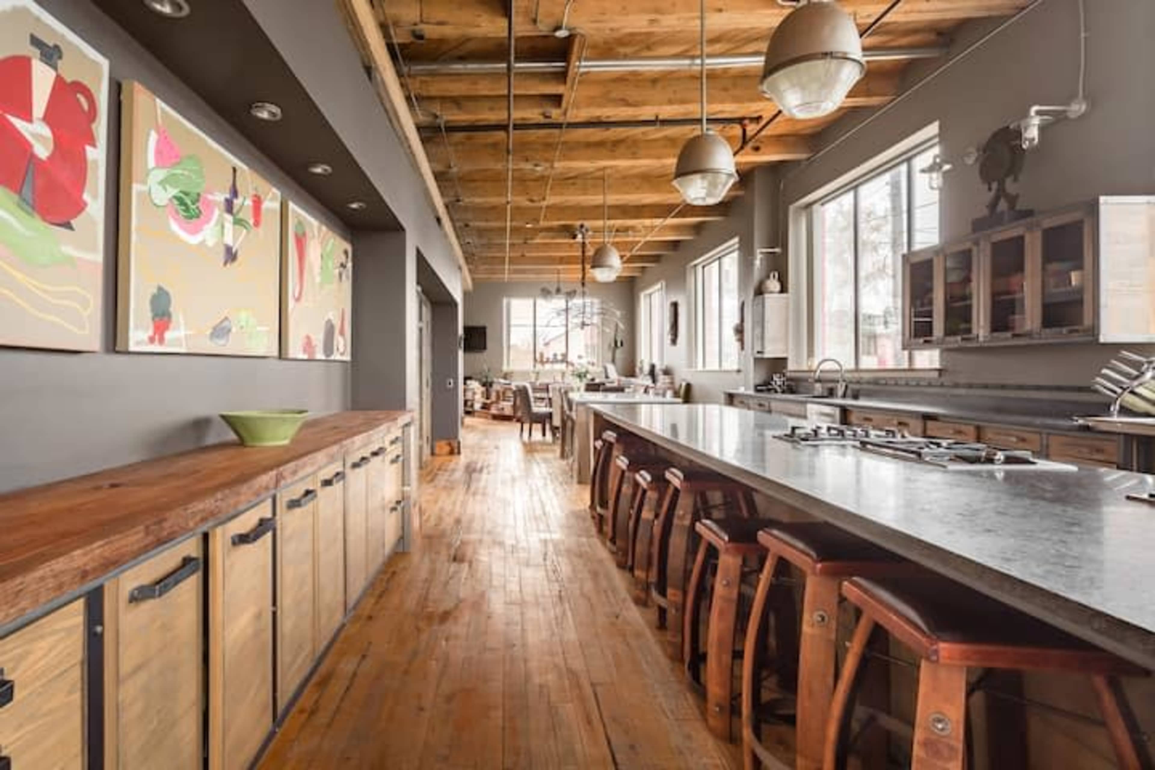 A spacious kitchen with a long countertop, wooden stools, and colorful artwork on the walls.