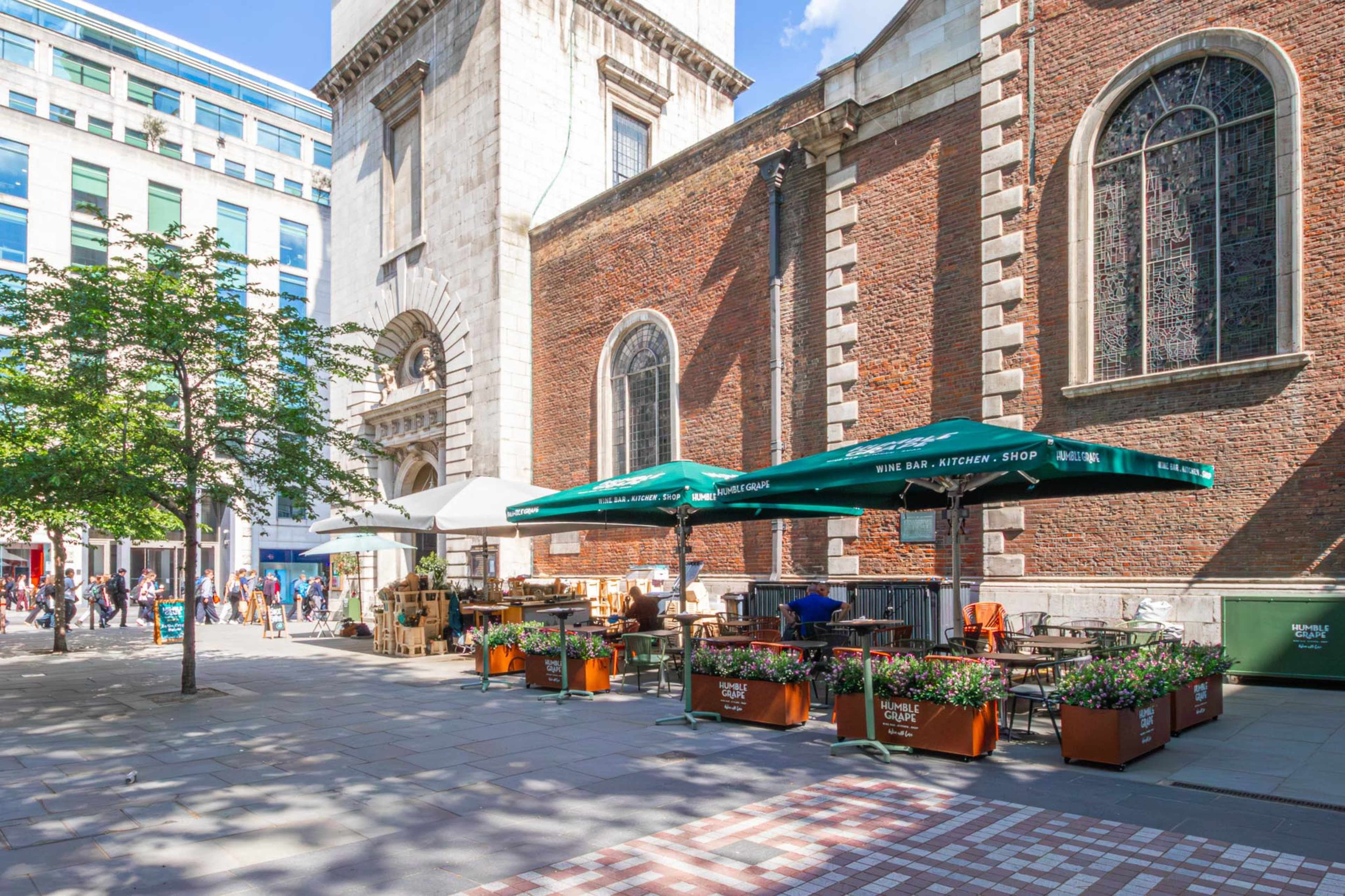 The image shows an outdoor café with umbrellas and planters set up near a historic brick building.