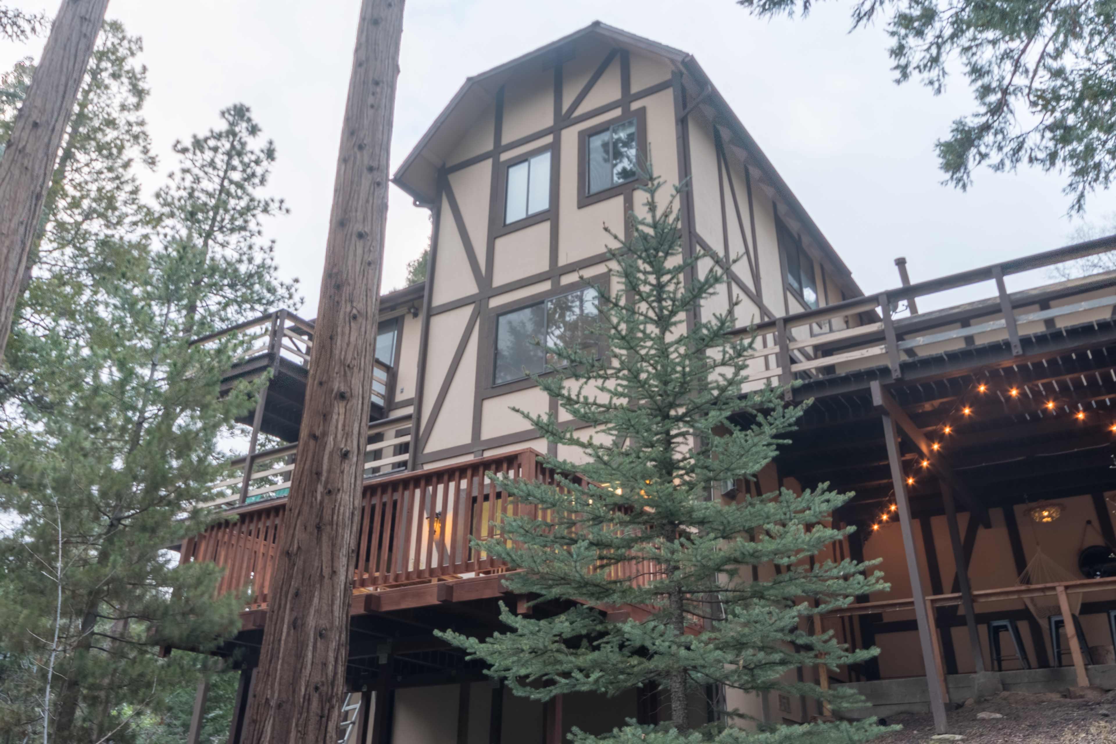 A tall, multi-level house with a distinctive architectural design surrounded by tall pine trees and outdoor lighting.