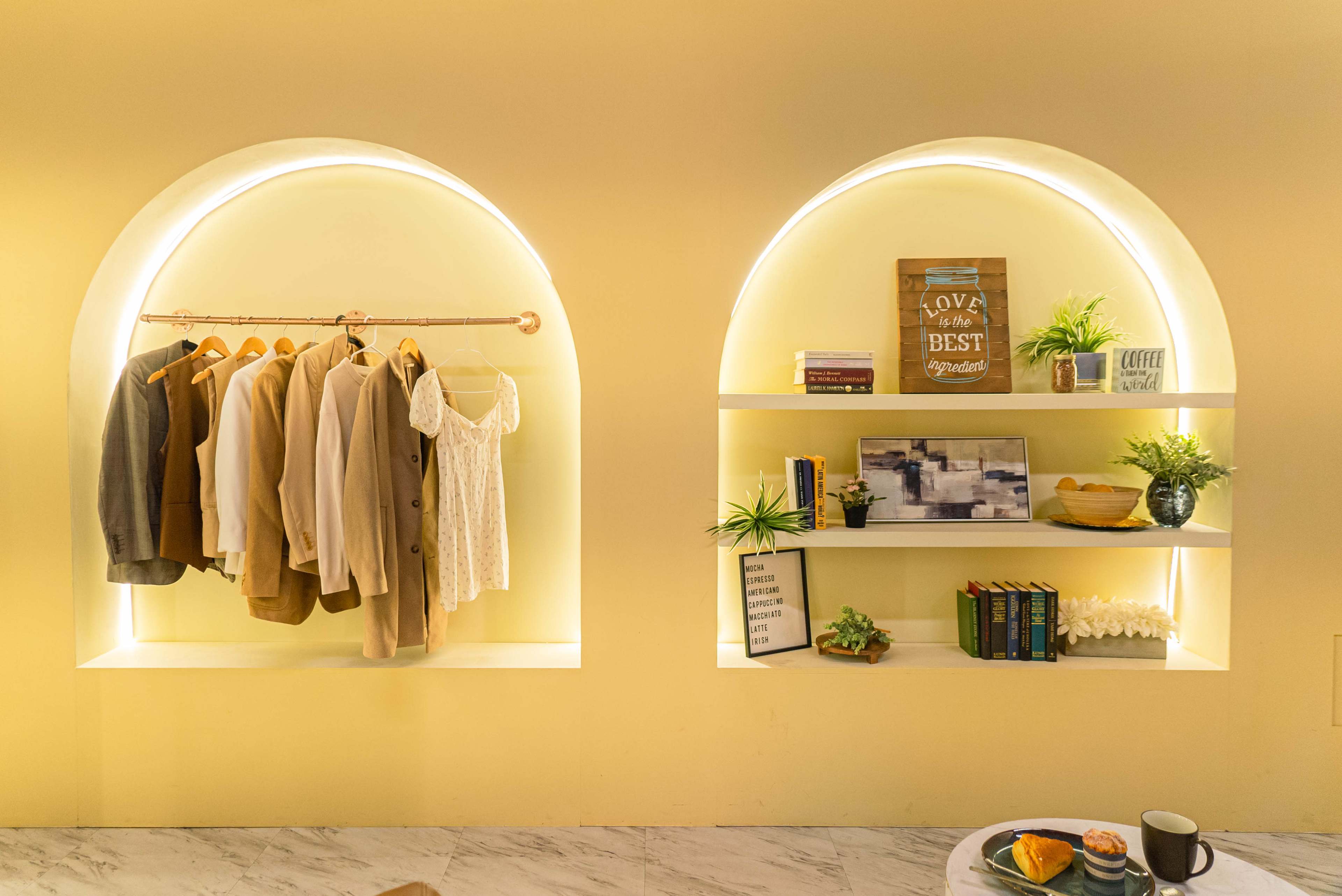 The image shows a room with two arched shelves; one side displays hanging clothes, while the other features books, plants, and decorative items.