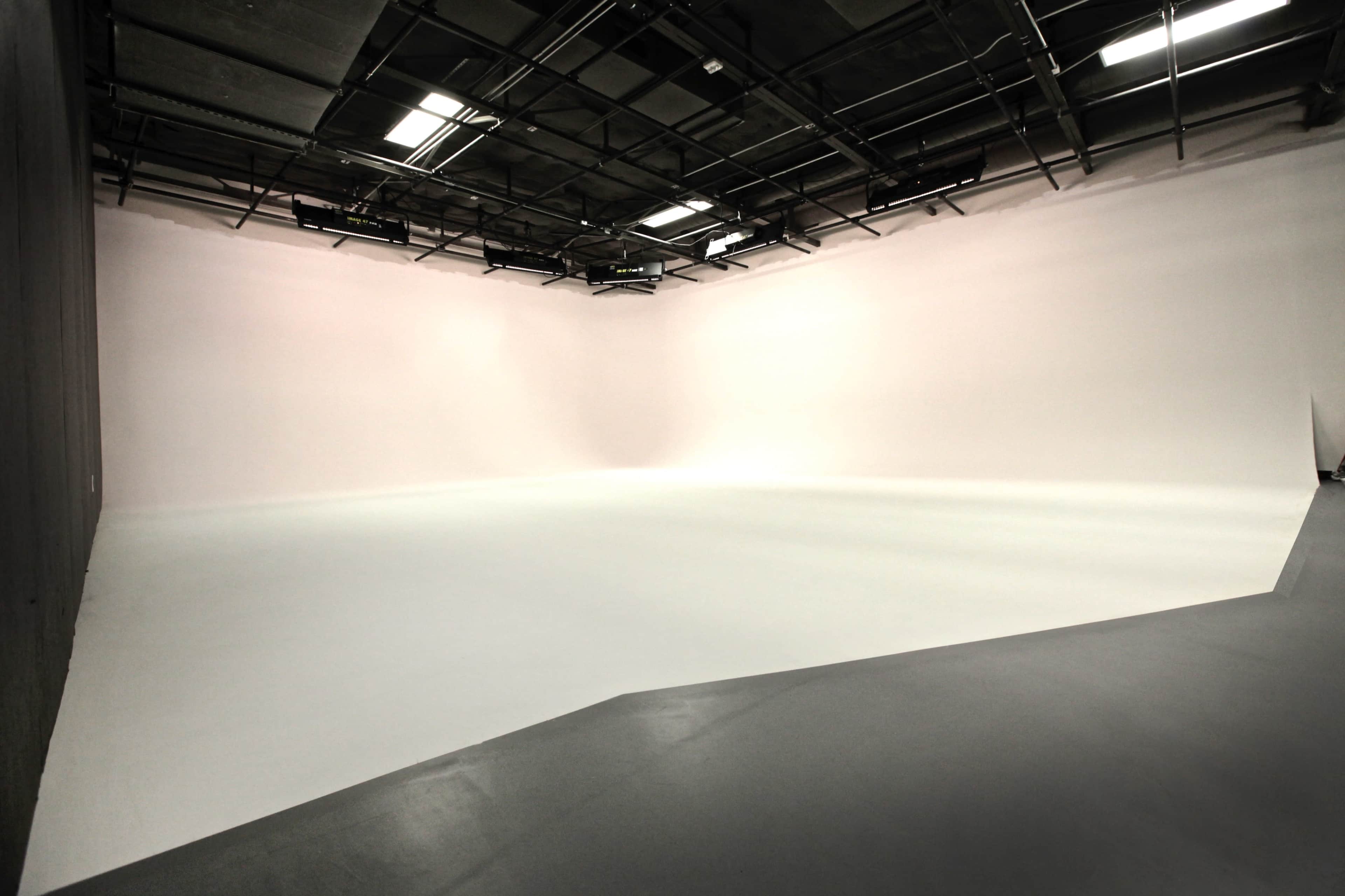 A large, empty studio space with a seamless white backdrop and a smooth floor.