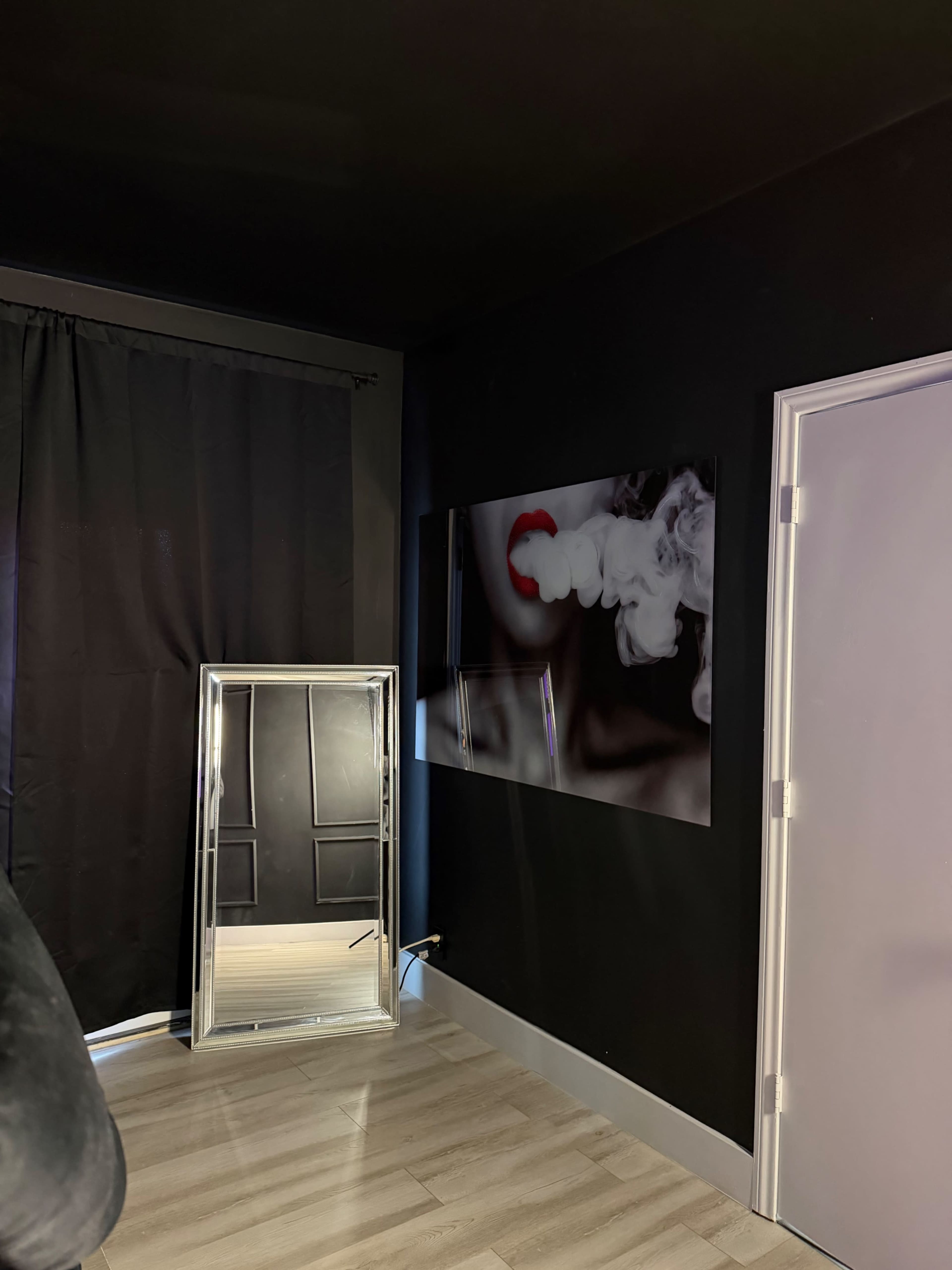 The scene features a dark room with a black wall, a mirrored cabinet leaning against one wall, and a picture of lips exhaling smoke mounted on another wall.