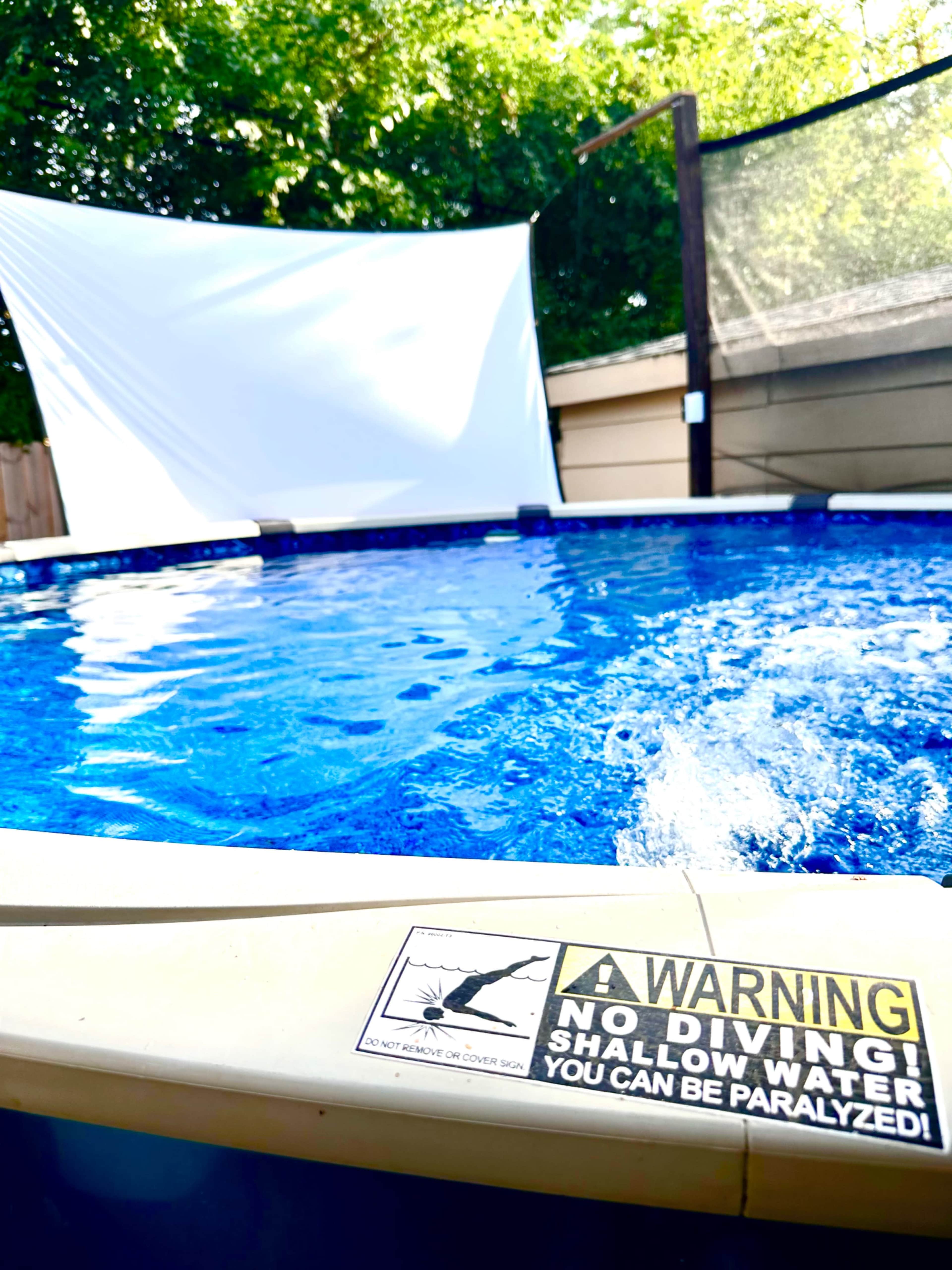 A swimming pool with a warning sign stating "No Diving! Shallow Water! You Can Be Paralyzed!" positioned beside it.