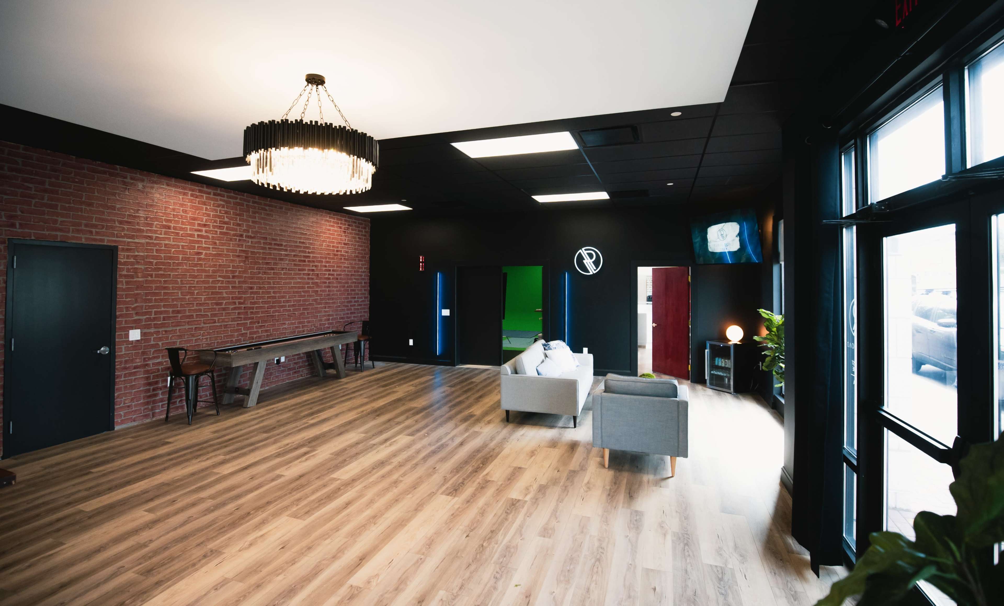 A spacious interior room with wooden flooring, exposed brick walls, a long table, modern seating, and two colored accent walls.